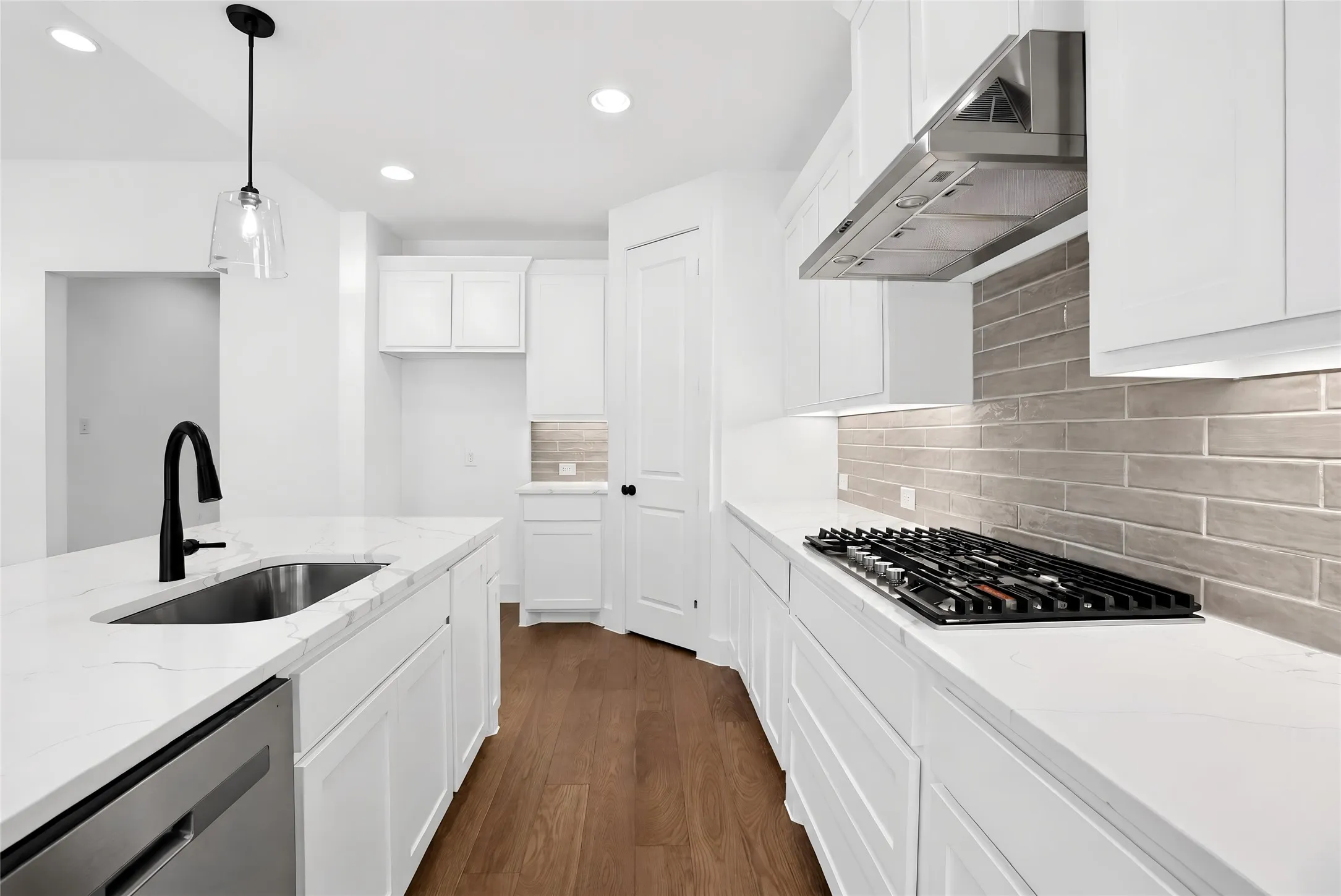 Kitchen featuring an island with a stainless steel sink, a gas cooktop, white cabinetry, light-toned subway tile backsplash, and wood-finish flooring