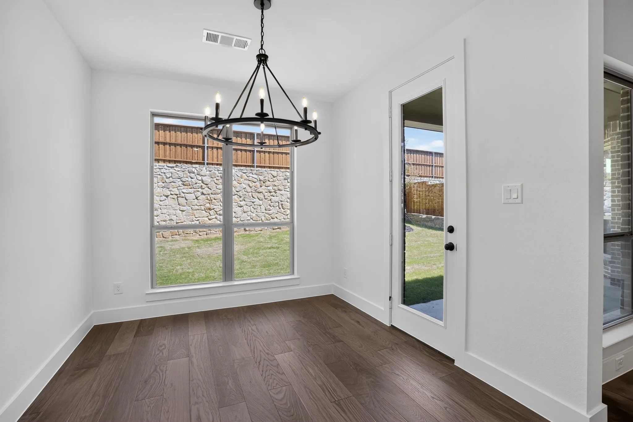 Wood-finish flooring, a contemporary black chandelier, and a full-light panel door