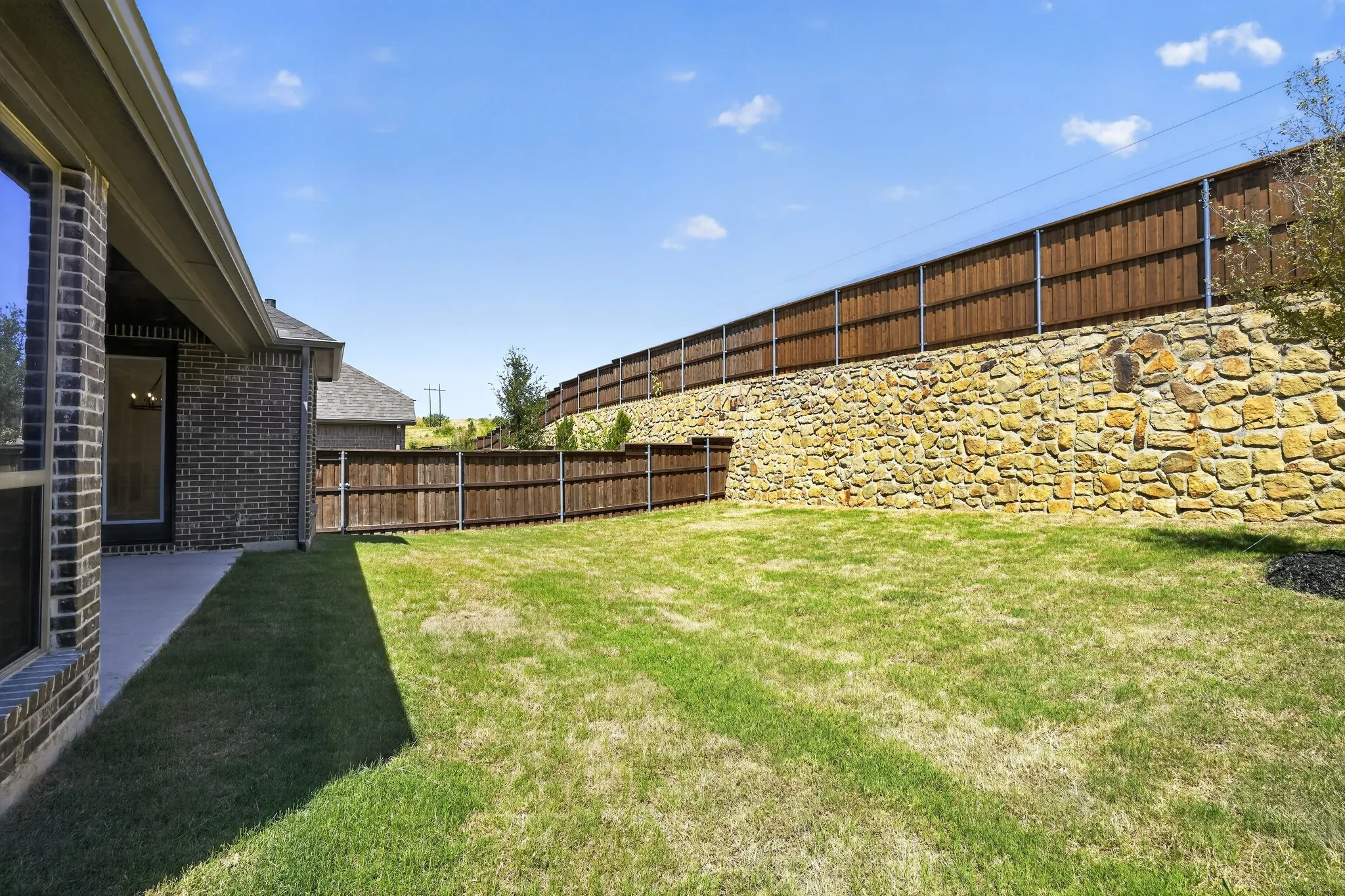 Expansive backyard featuring a stone retaining wall, wood fencing, and a concrete patio
