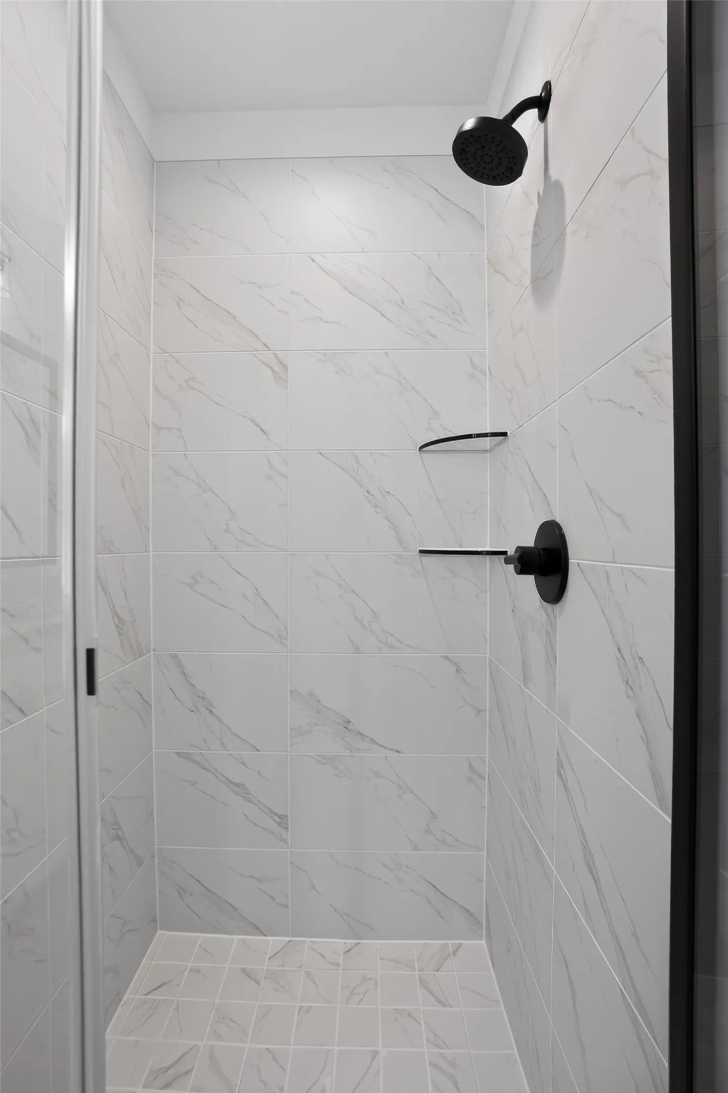 Enclosed shower with large format wall tile, matte black fixtures, built-in shelving, and a glass enclosure