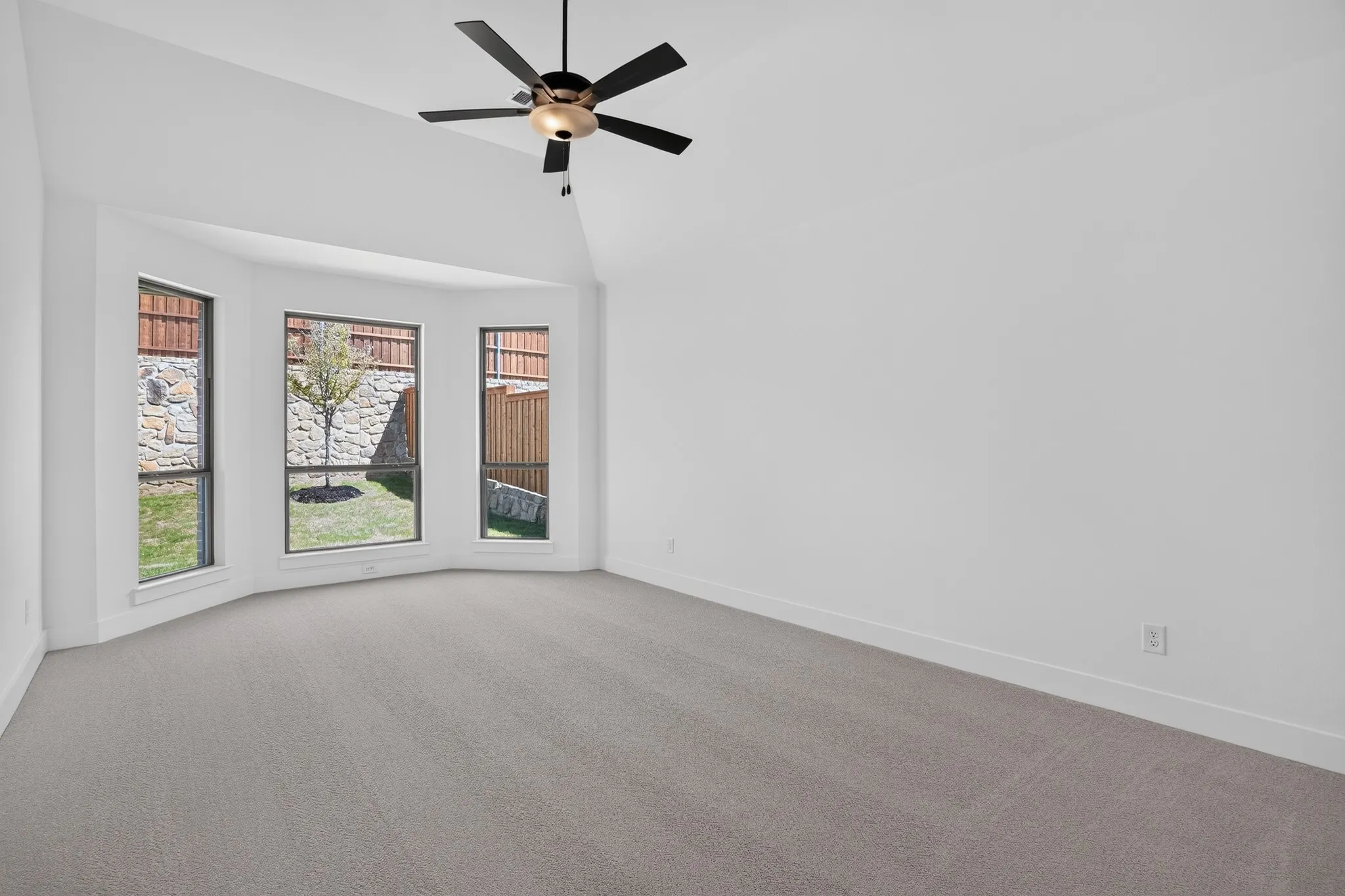 Vaulted ceiling with a ceiling fan, bay windows, and neutral carpeting