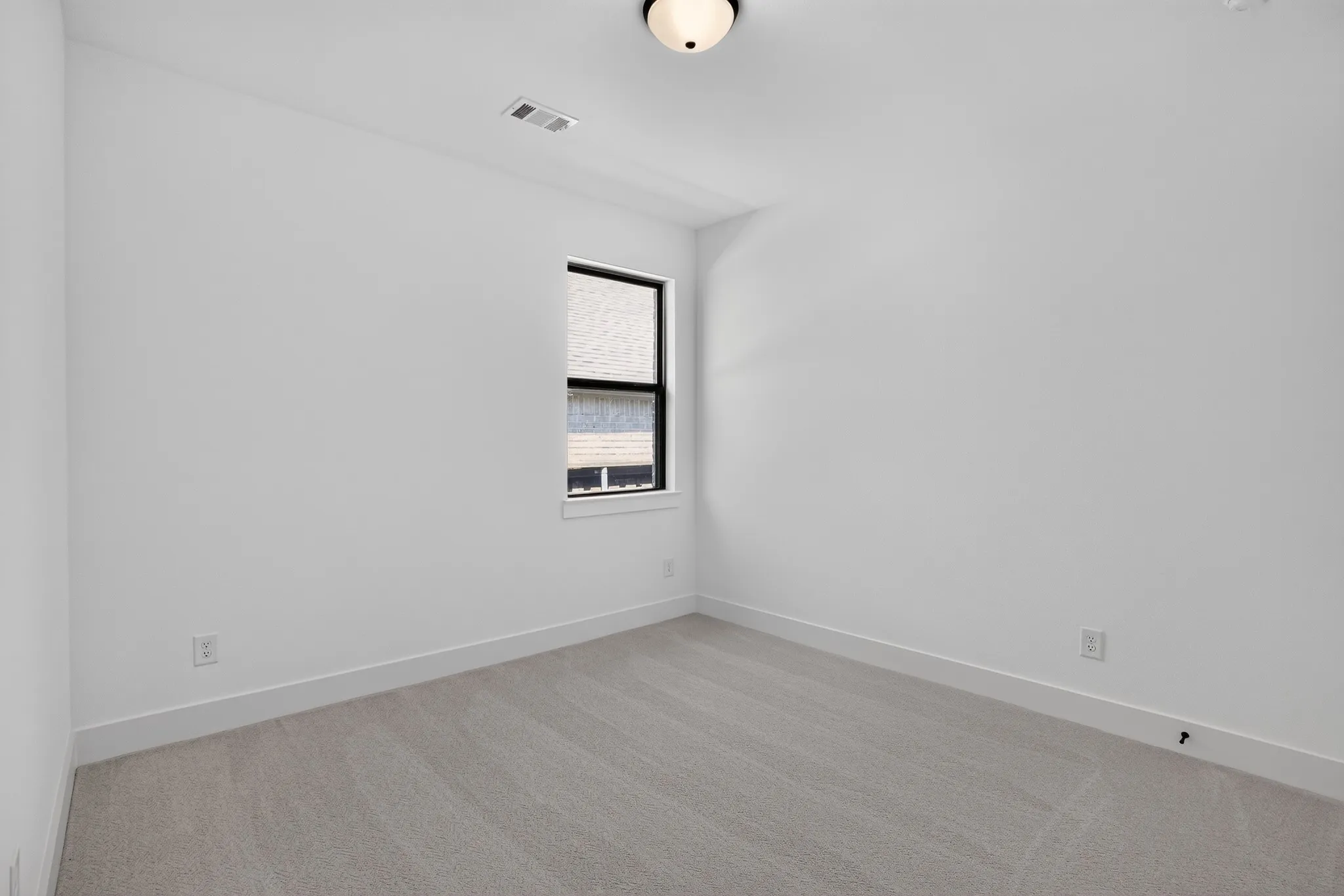 Neutral-toned carpet flooring, white painted walls, and a single black-framed window