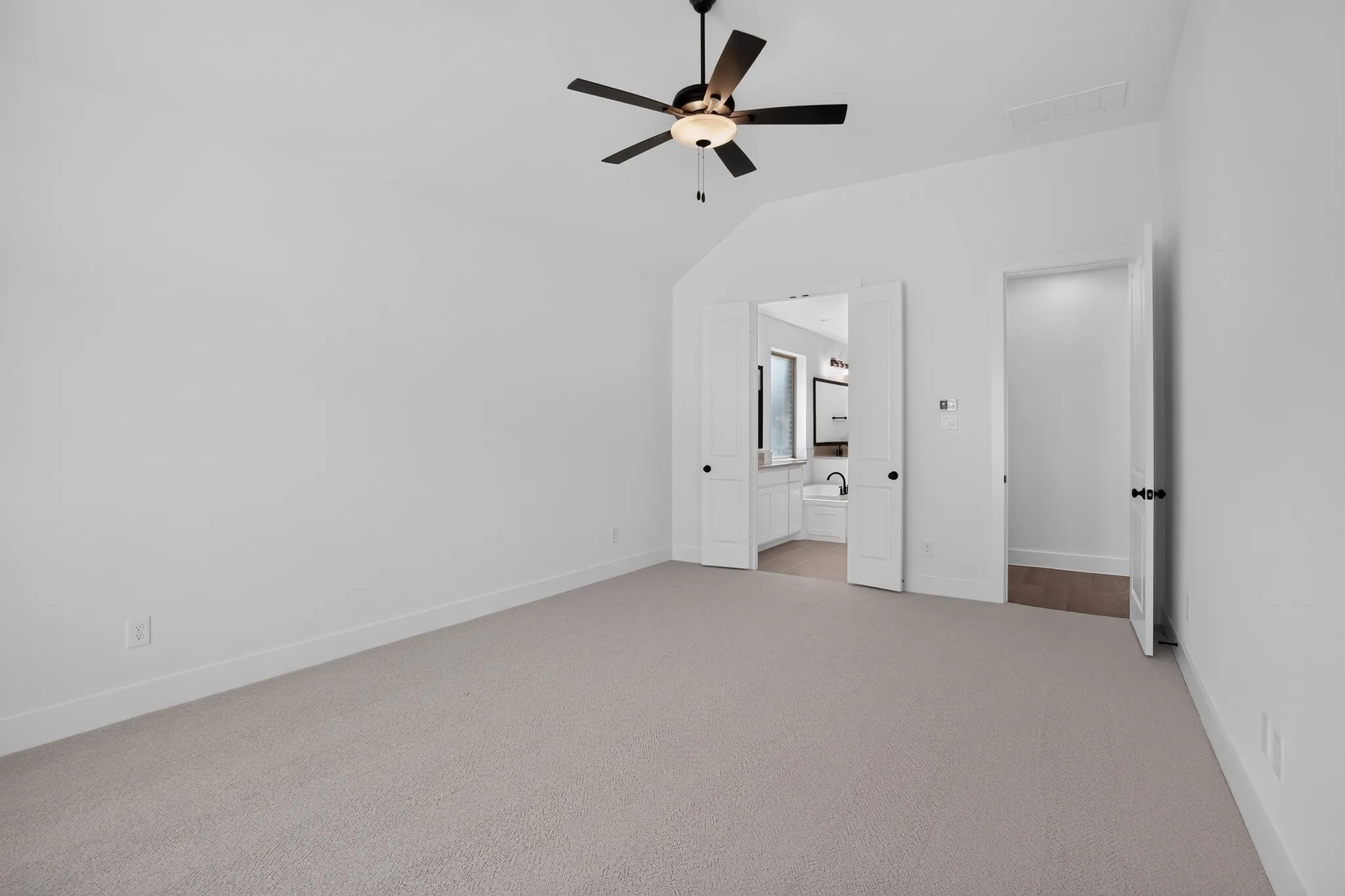 Carpeted room featuring a vaulted ceiling with a ceiling fan, a white paneled door, and bi-fold doors leading to a bathroom with a window