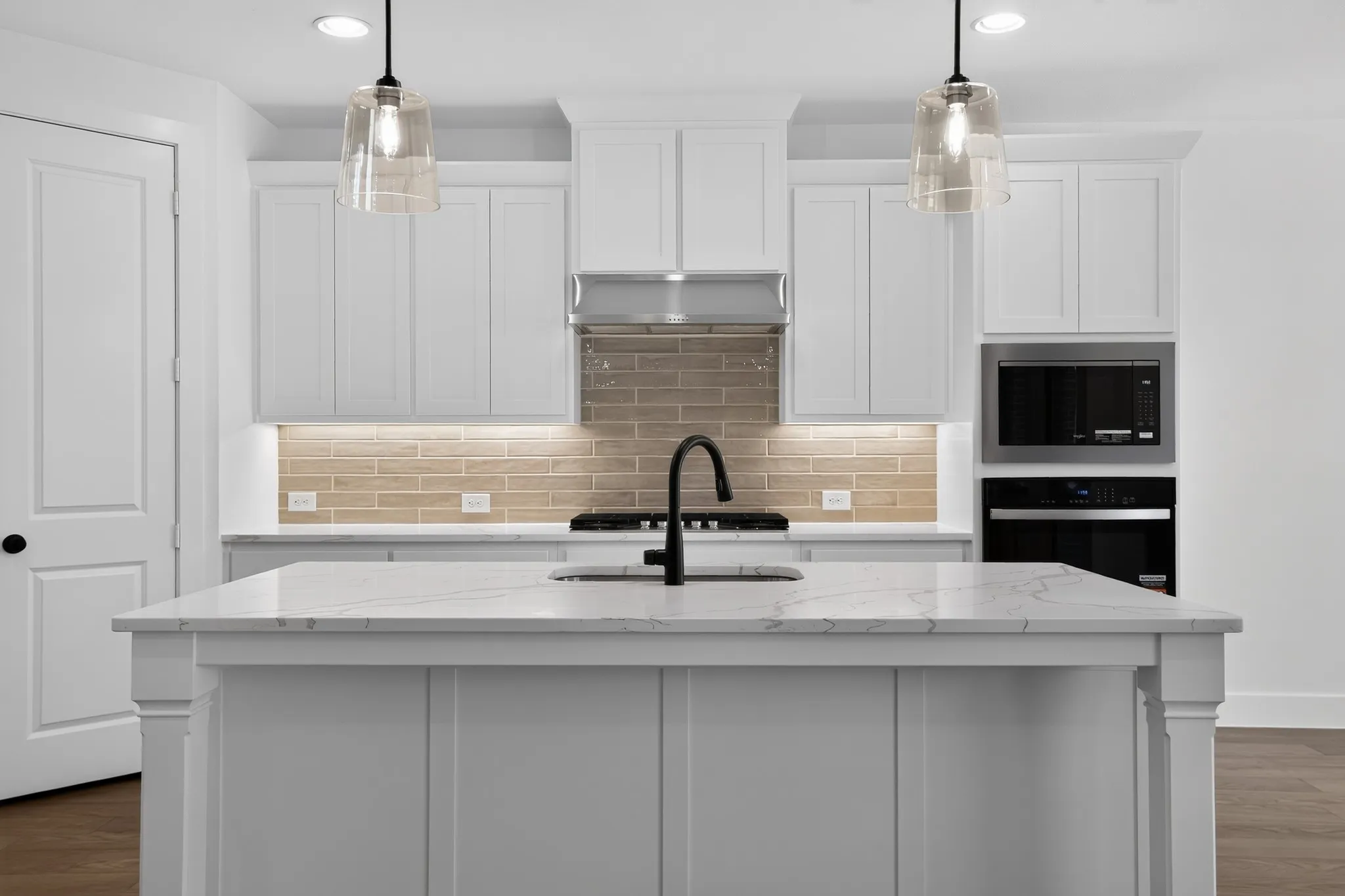 Central island with a white countertop and integrated sink, white cabinetry, integrated stainless steel appliances, brick-patterned backsplash, and pendant lighting