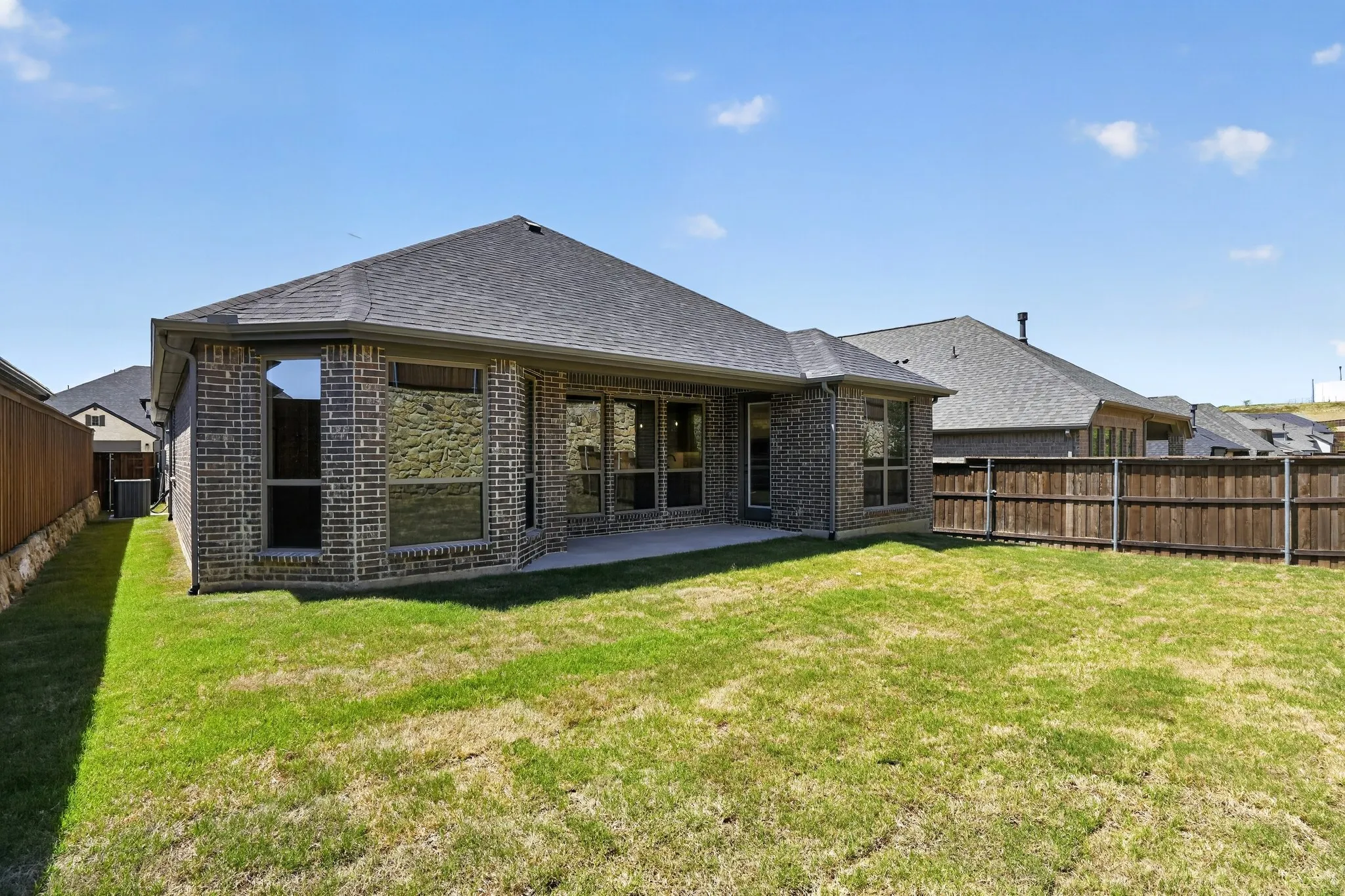Expansive backyard with a manicured lawn, brick exterior, dark shingle roof, and a privacy fence
