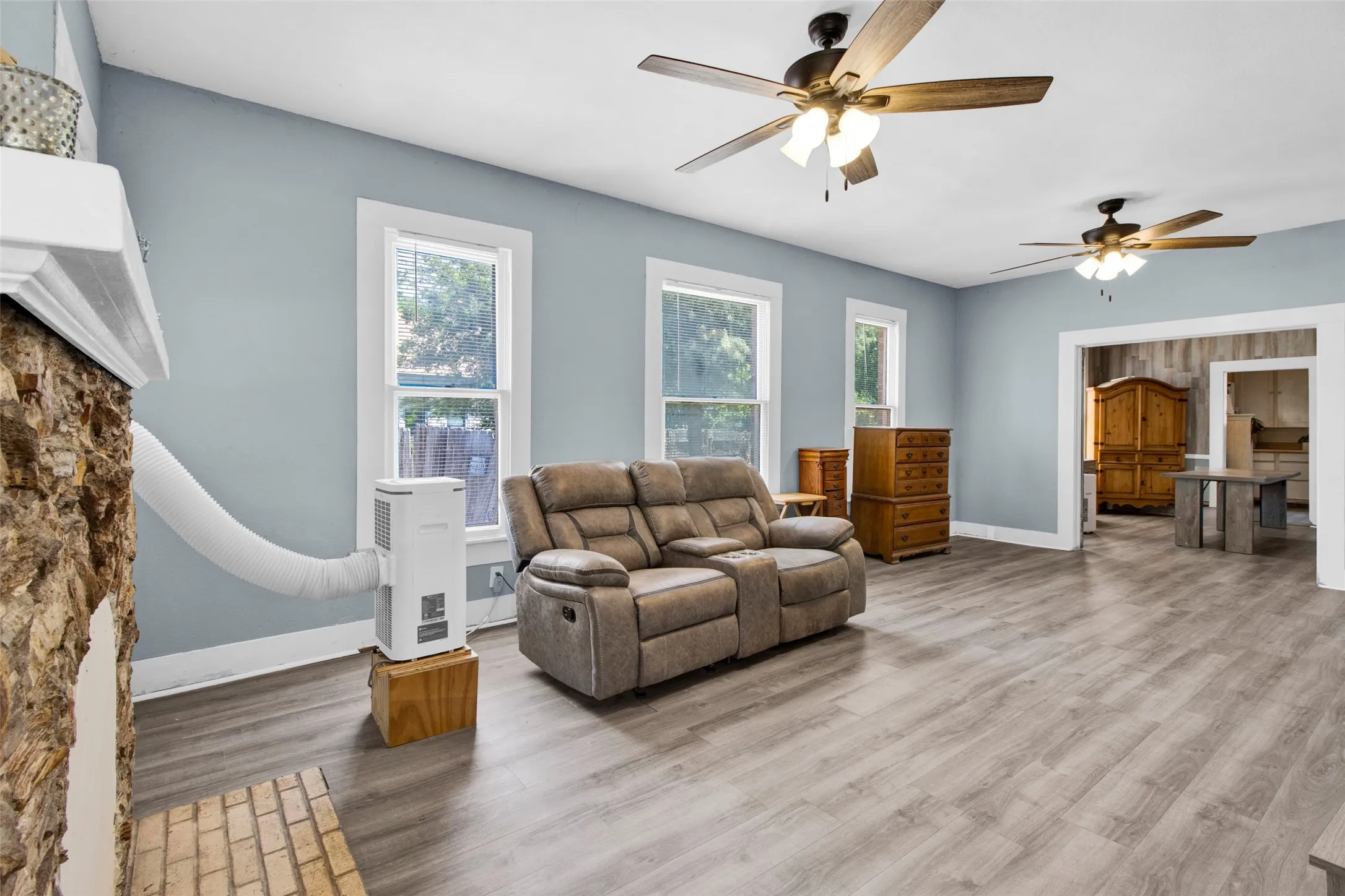 Spacious room featuring wood-finish flooring, light blue wall paint, and multiple ceiling fans