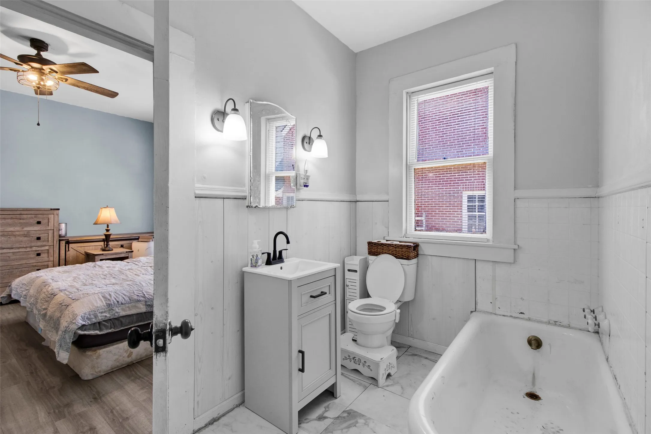Bathroom featuring a single vanity with matte black faucet, wall-mounted light fixtures, a white toilet, and a bathtub