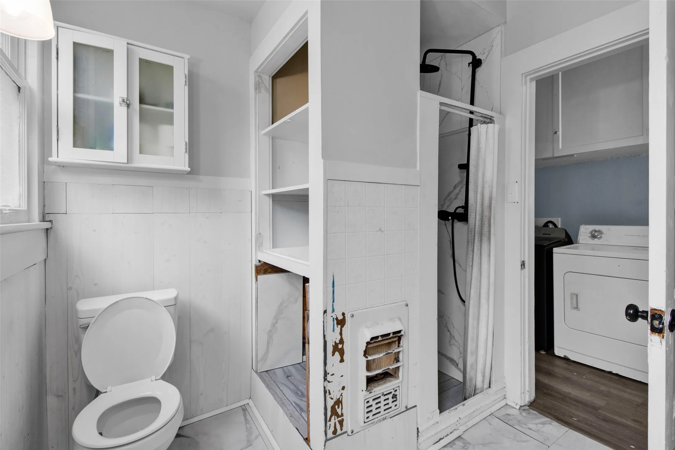 Bathroom featuring a shower with black fixtures and a tile surround, white wainscoting, and a wall-mounted cabinet