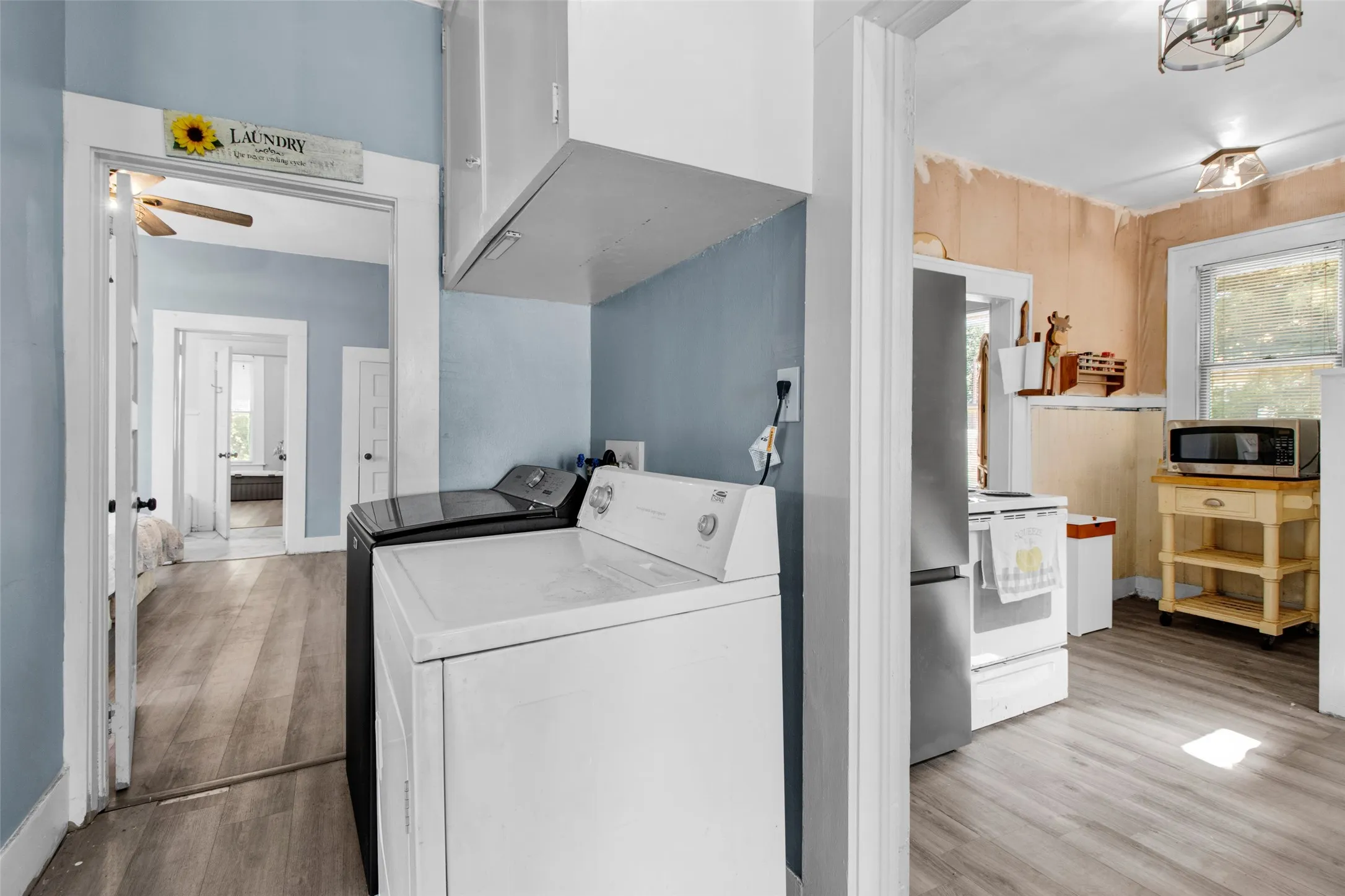 Dedicated laundry area featuring a light blue wall, white upper cabinetry, and wood-finish flooring