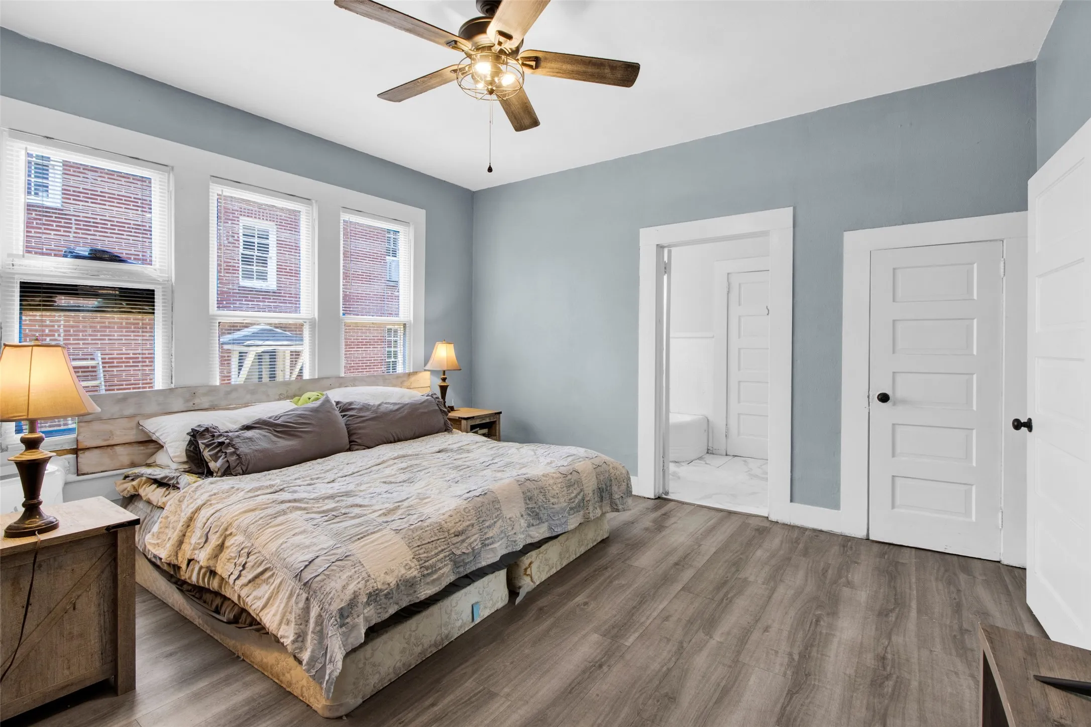 Spacious room with wood-finish flooring, three large windows, a ceiling fan, and painted walls