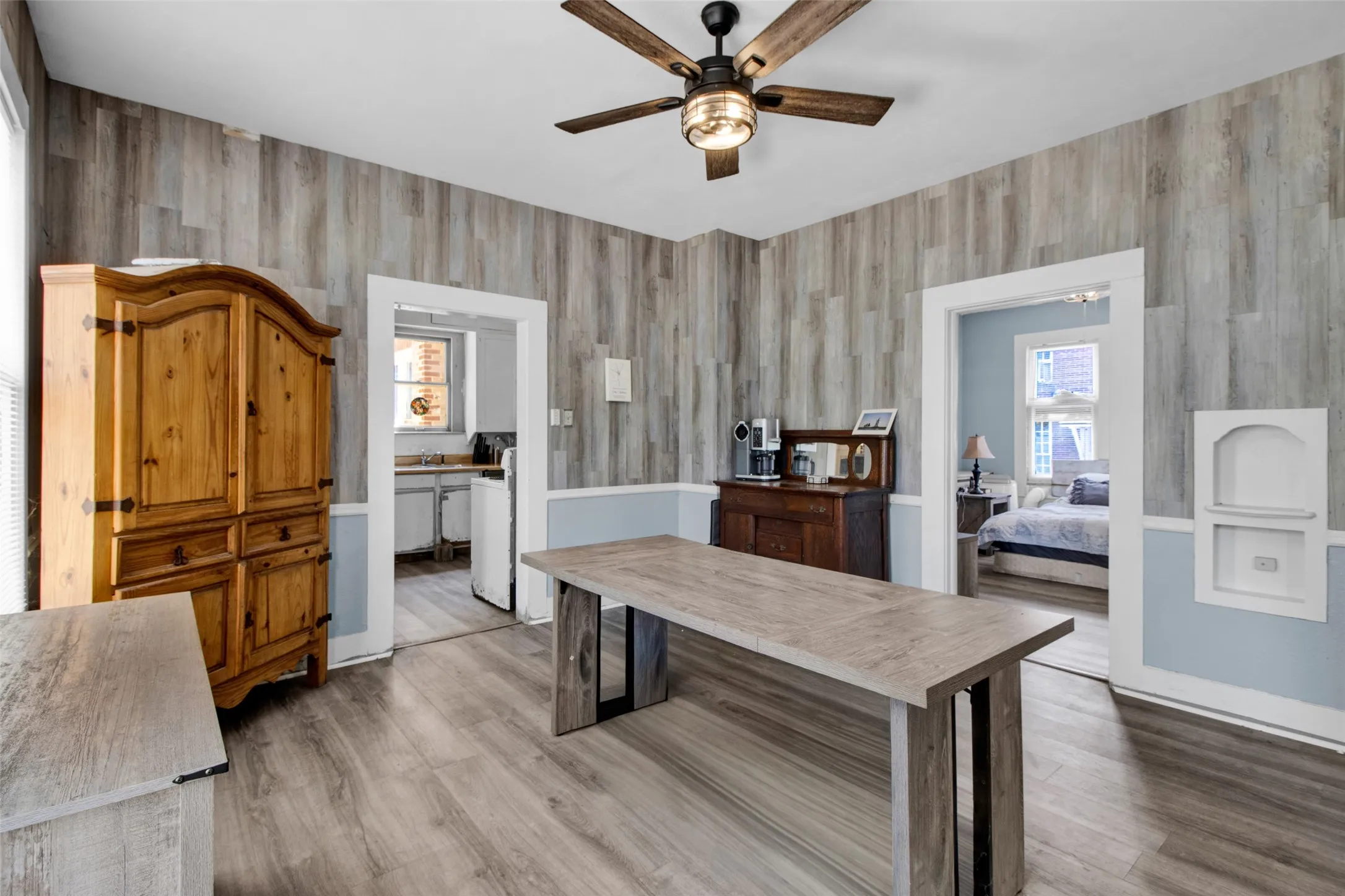 Open-concept room featuring wood-finish flooring, accent wall paneling, a ceiling fan with integrated lighting, and white trim work