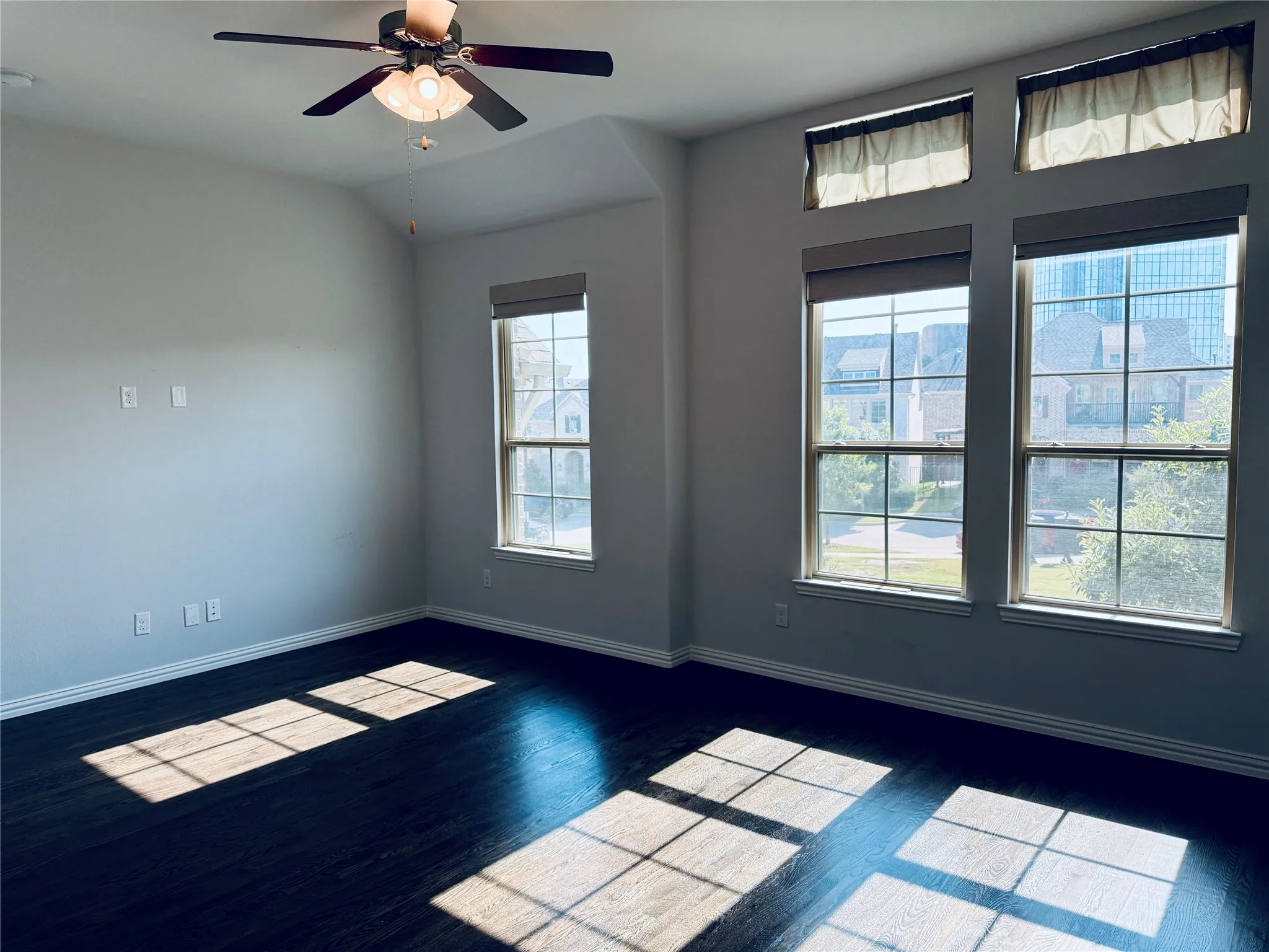 Spacious room featuring dark wood-finish flooring, light neutral-toned walls, and a motorized blinds