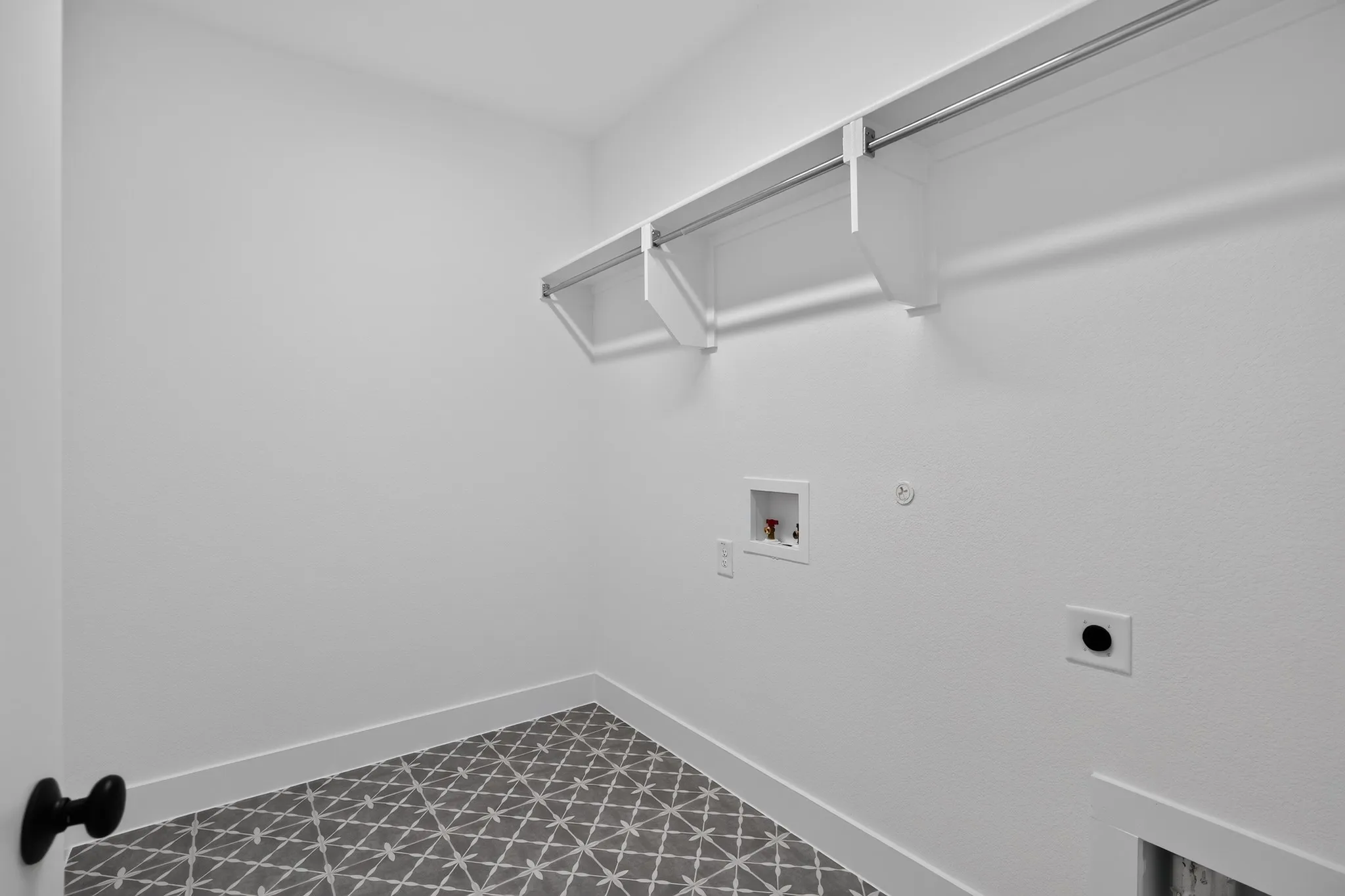 Laundry area featuring geometric patterned tile flooring, a built-in hanging rod, and utility hookups
