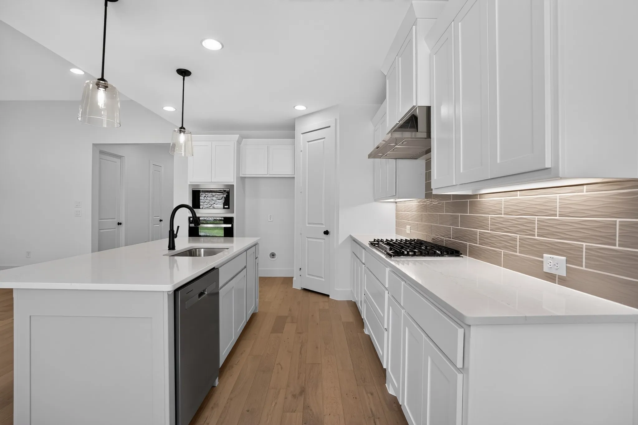 Kitchen featuring an island with sink, white shaker cabinetry, white countertops, wood-finish flooring, and a gas cooktop with an overhead range hood