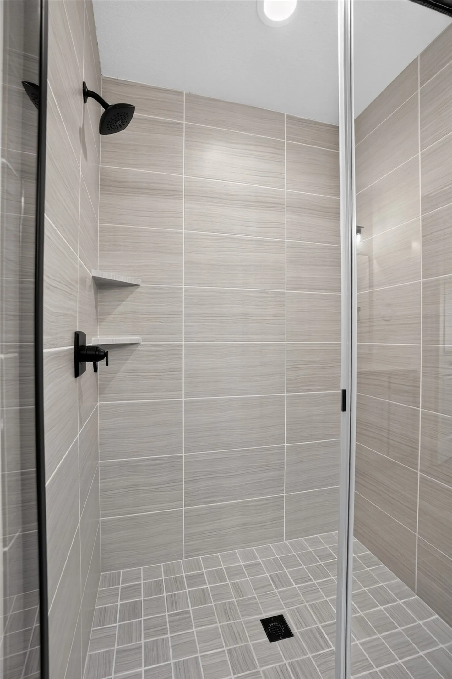 Shower enclosure featuring light-toned large format tile, a tile-in shower niche, and matte black fixtures