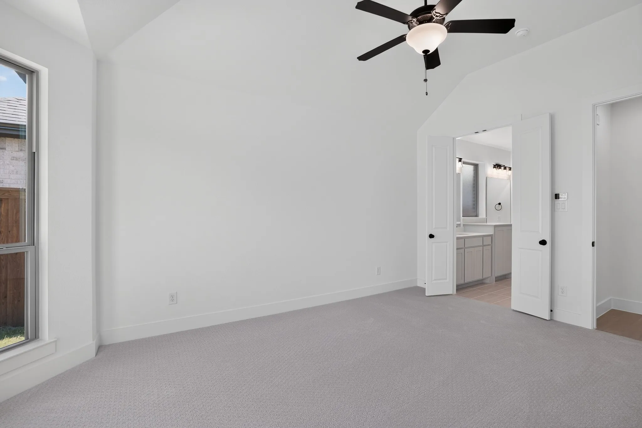 Vaulted ceiling with an attached ceiling fan, light gray carpet, and a large window