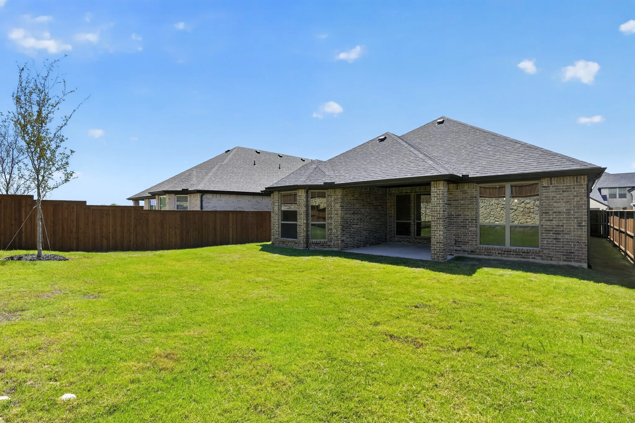 Expansive grassy backyard featuring a full privacy fence, covered patio, and brick exterior