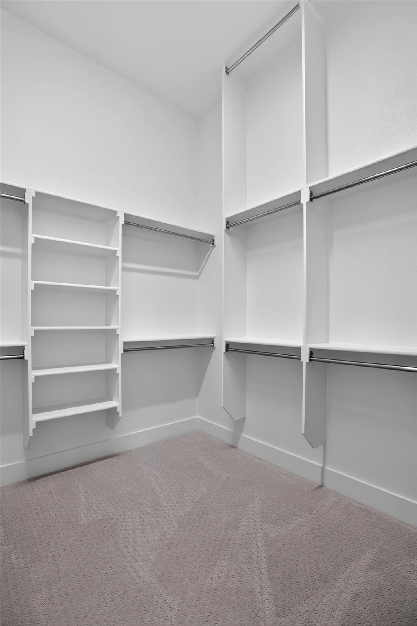 Built-in closet system featuring white shelving, multiple hanging rods, and light-colored carpeting