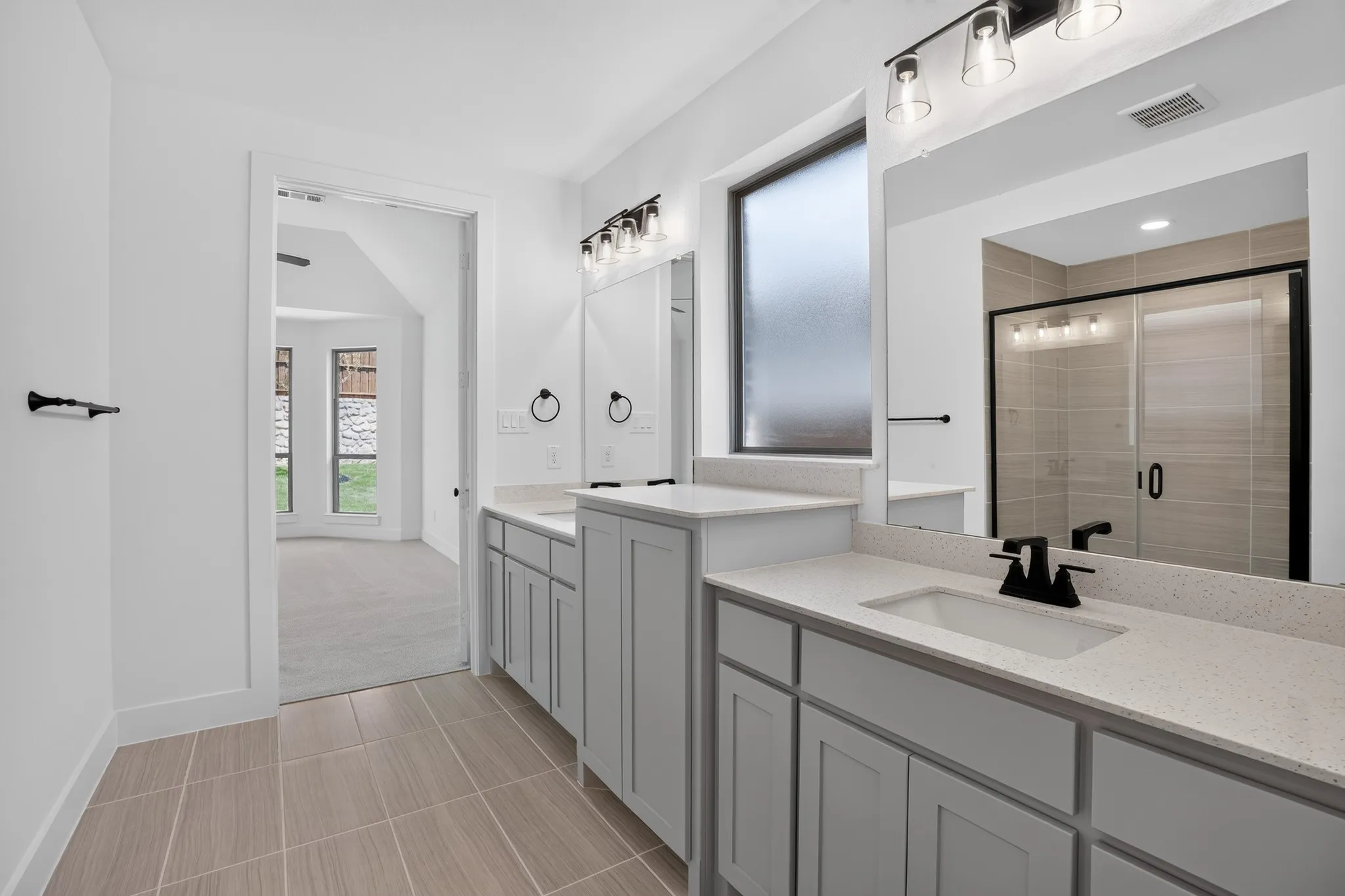 Primary bathroom suite featuring dual vanities with quartz countertops, gray cabinetry with integrated storage, vessel sinks with matte black fixtures, large framed mirror, and walk-in shower with glass enclosure and tile surround