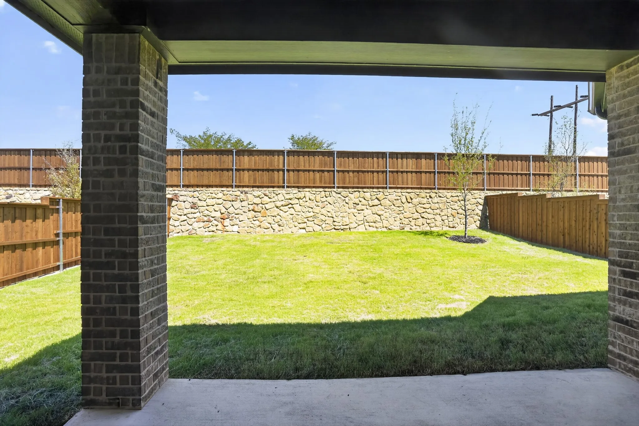 Outdoor patio with concrete flooring, brick columns, and a grassy yard