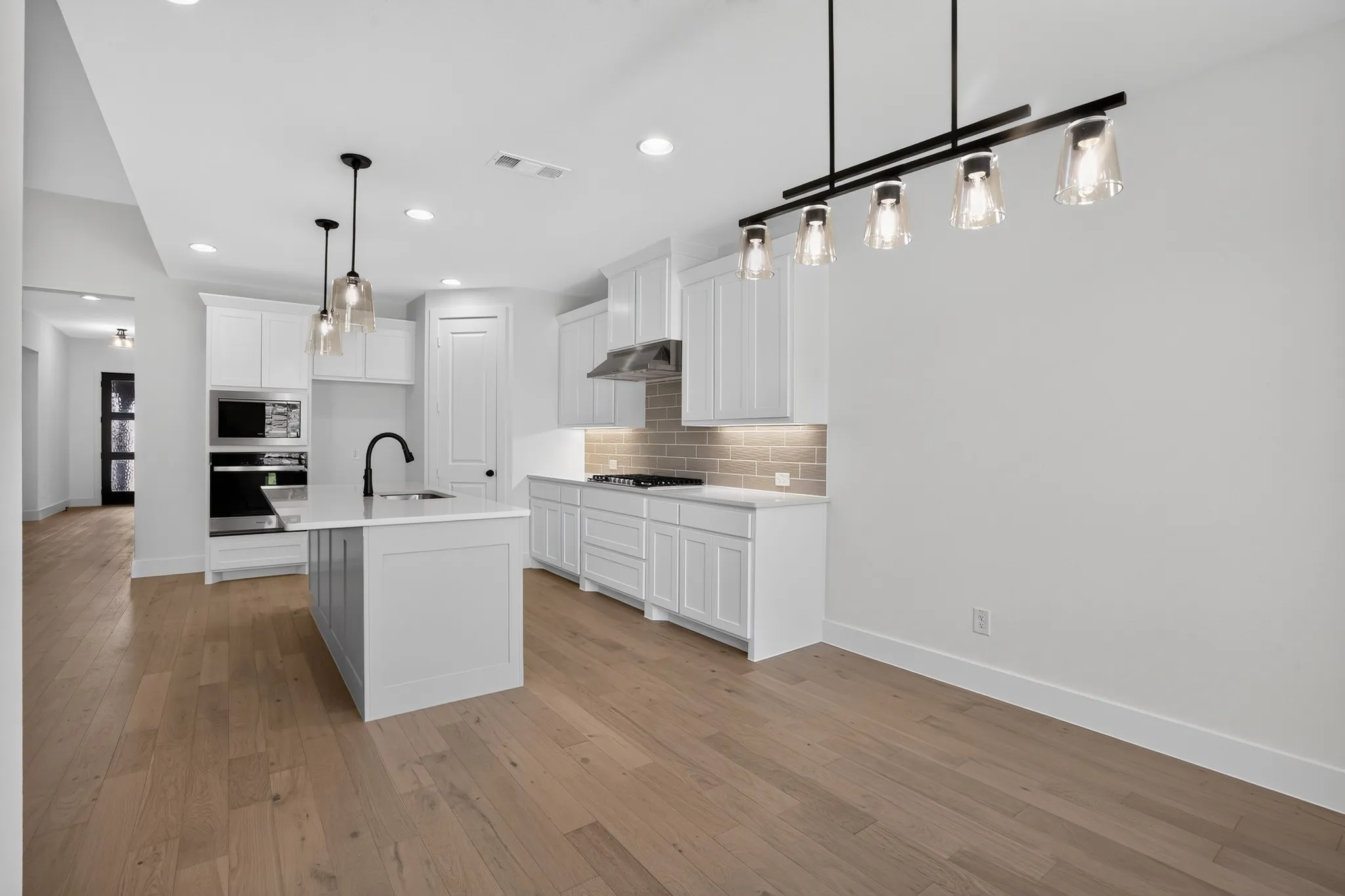 Open-concept kitchen featuring an island with sink, stainless steel appliances, light wood-finish flooring, white cabinetry, and recessed lighting