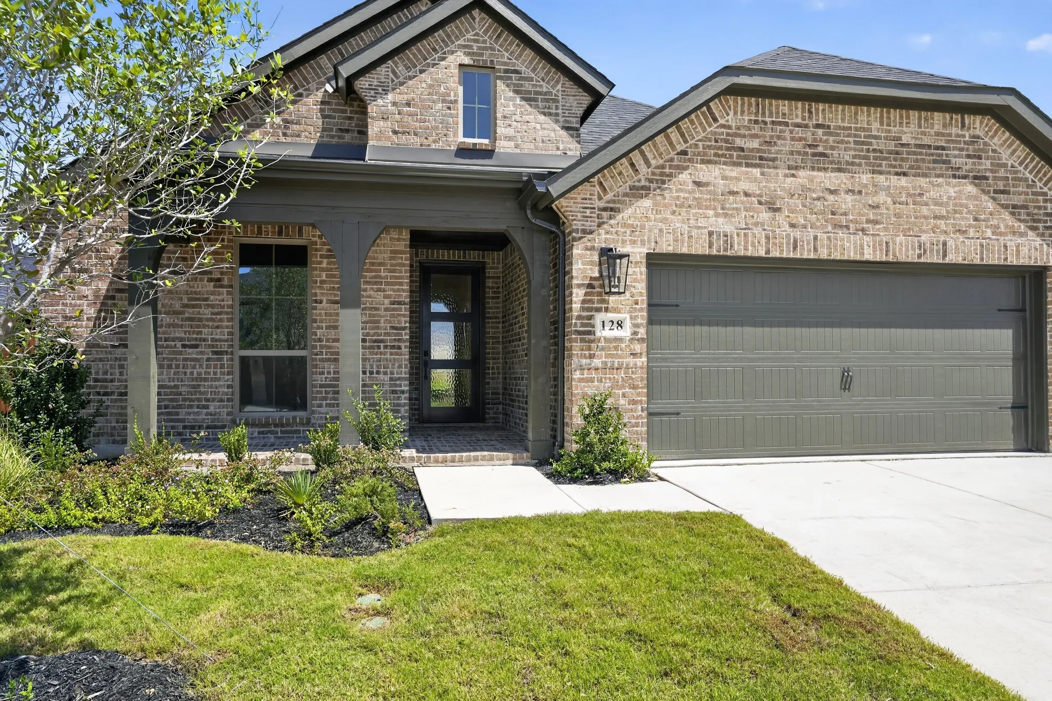 Brick exterior with a covered entry, an attached garage, and a concrete driveway