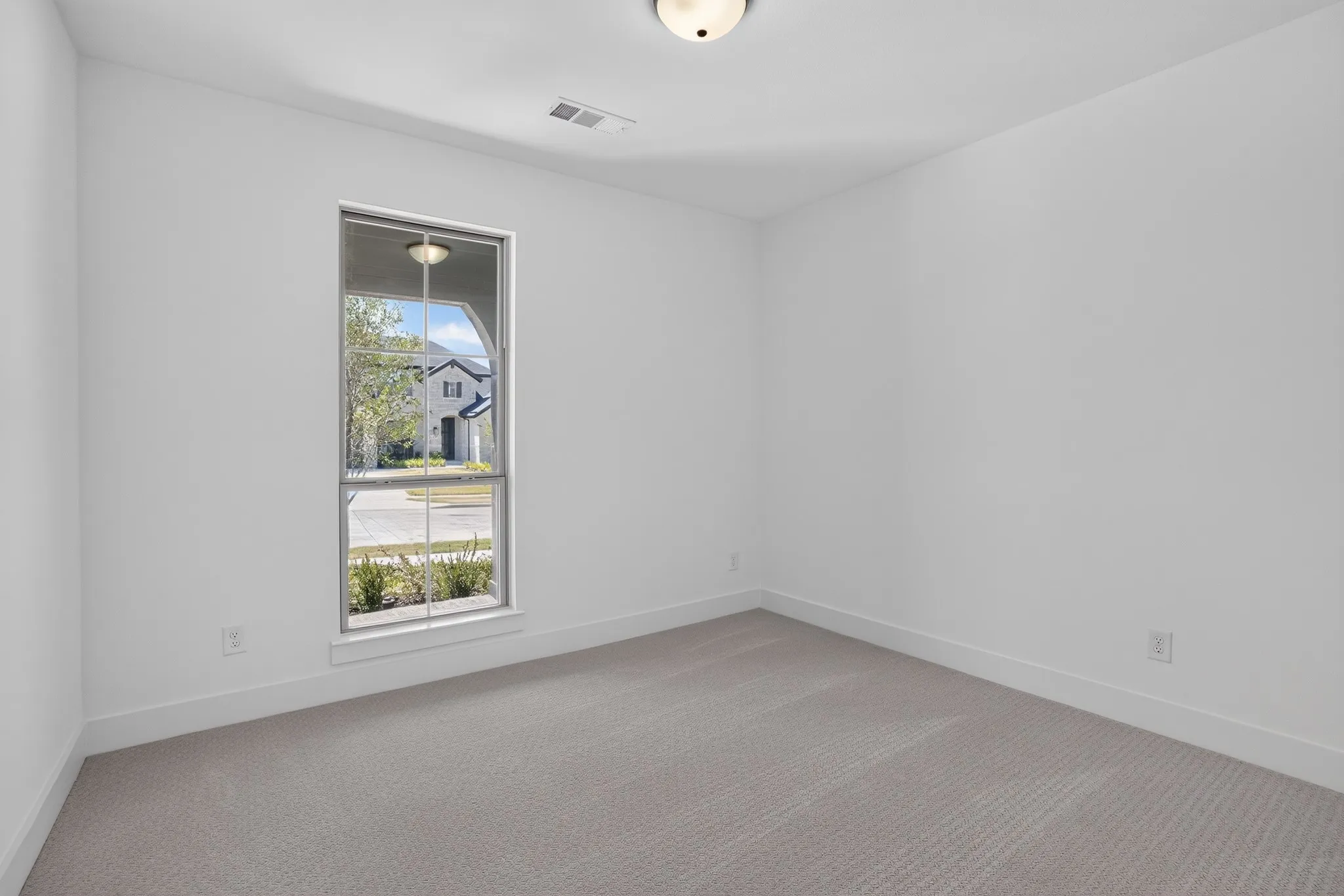 Window with exterior landscaping, light gray patterned carpet, white baseboards, and a flush mount ceiling light