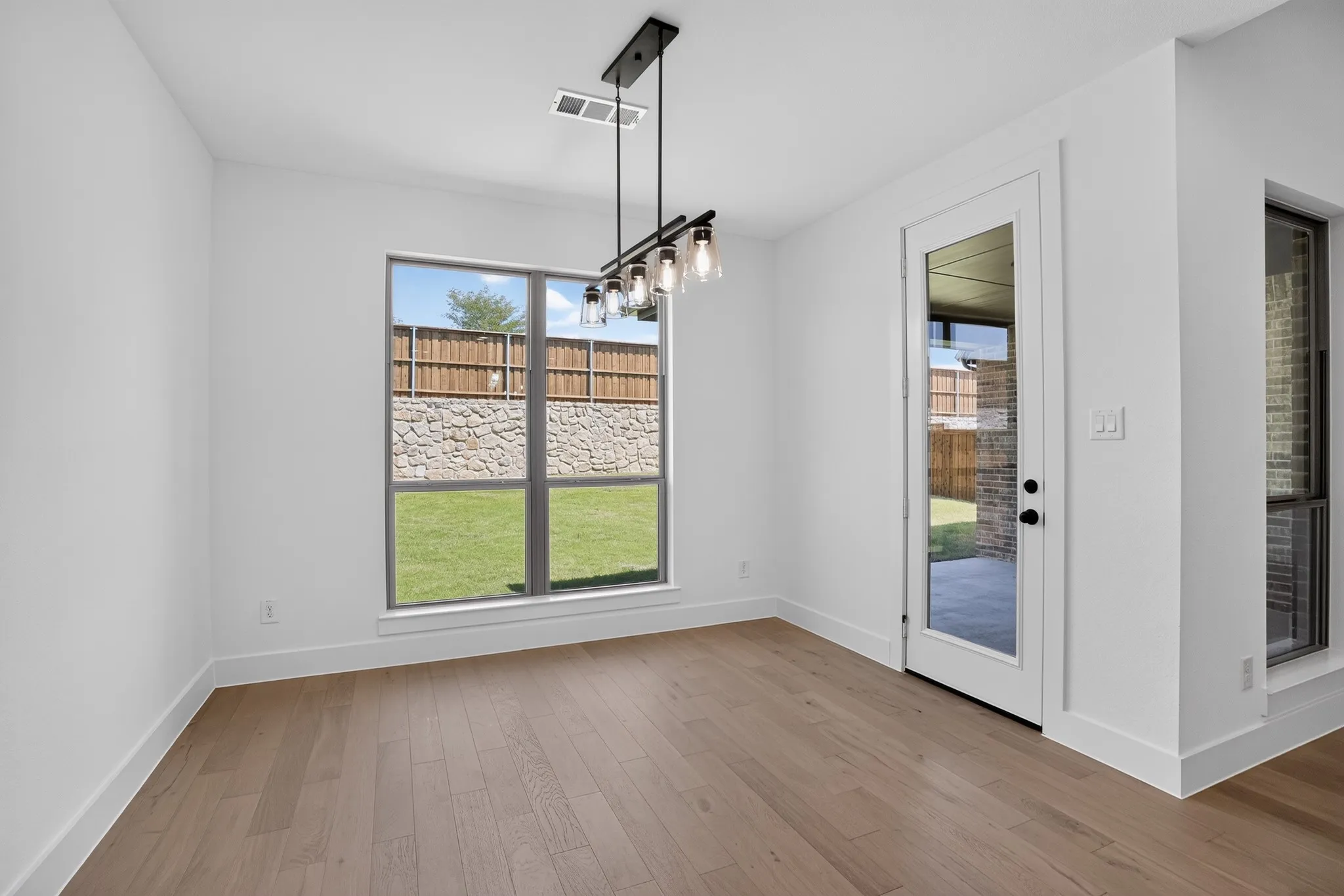 Wood-finish flooring, contemporary chandelier, full-light exterior door, and a large window overlooking the backyard