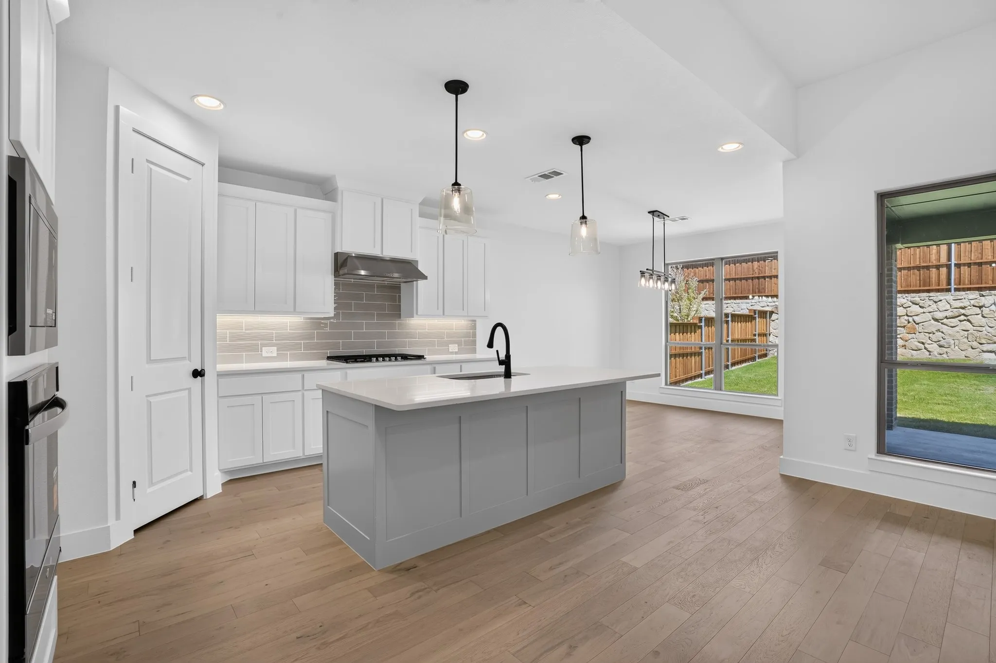 Kitchen featuring a light gray island with a white countertop, wood-finish flooring, white cabinetry, a gray subway tile backsplash, and stainless steel appliances