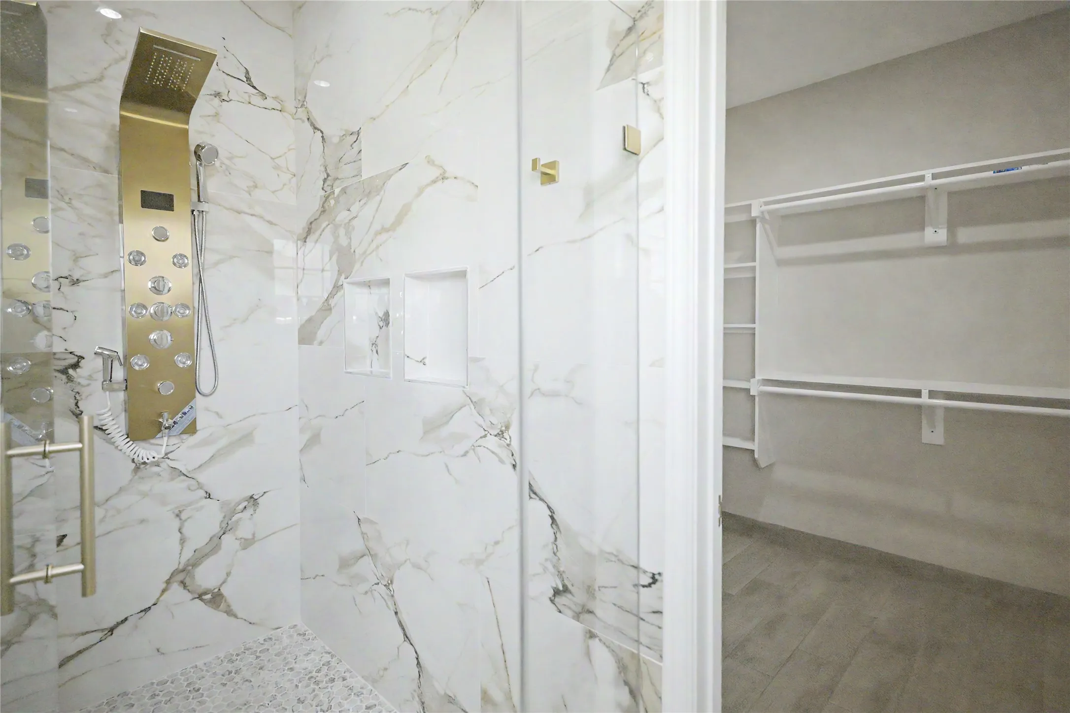 Walk-in shower featuring a gold-finish shower panel with body jets, white marble-look wall tiling, and a mosaic tile floor