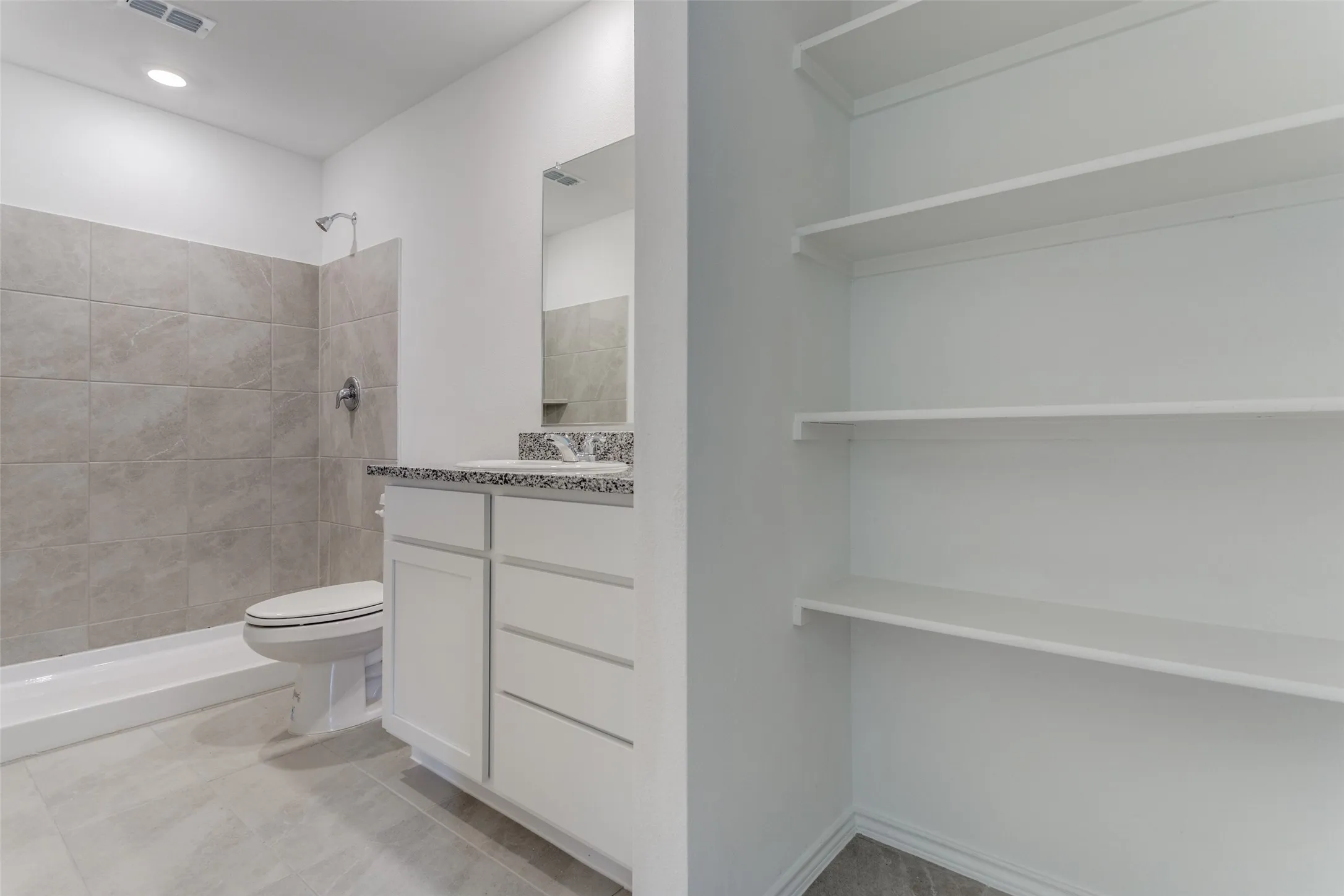 Bathroom featuring tiled shower, toilet, tile floors, and vanity