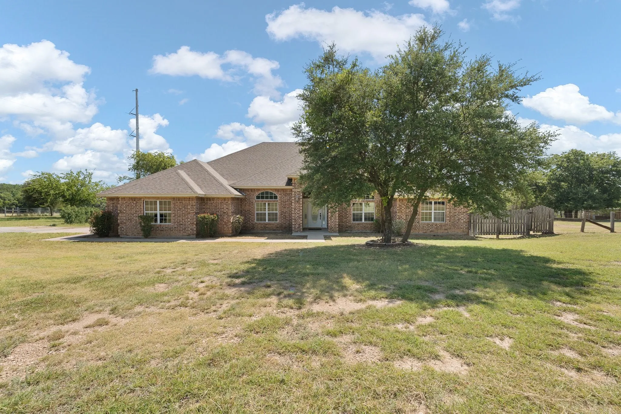 Brick exterior residence featuring a gabled roofline, multiple windows, and an established front yard with mature landscaping