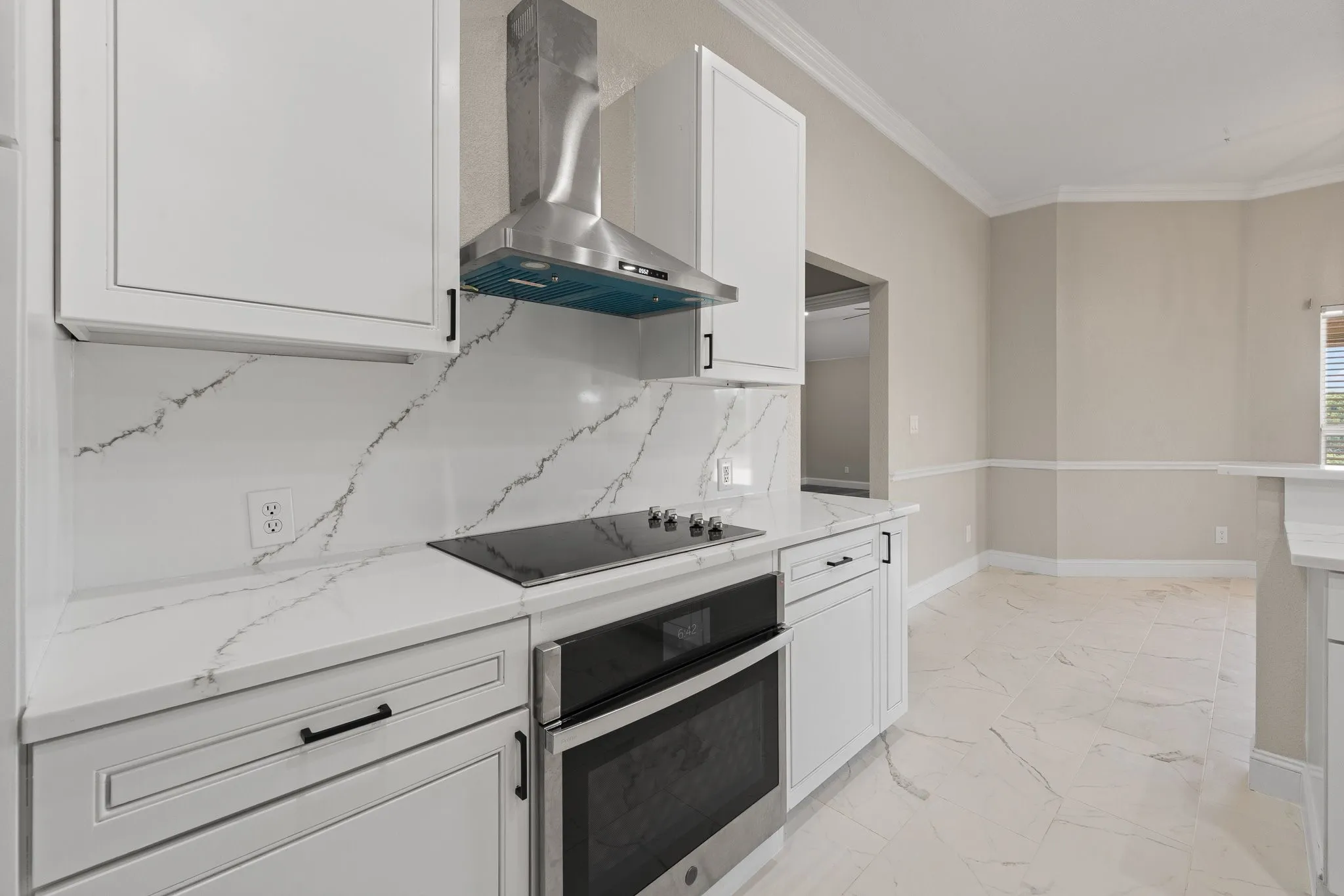 Modern kitchen featuring white cabinetry, a stainless steel range hood, built-in oven, and a sleek cooktop
