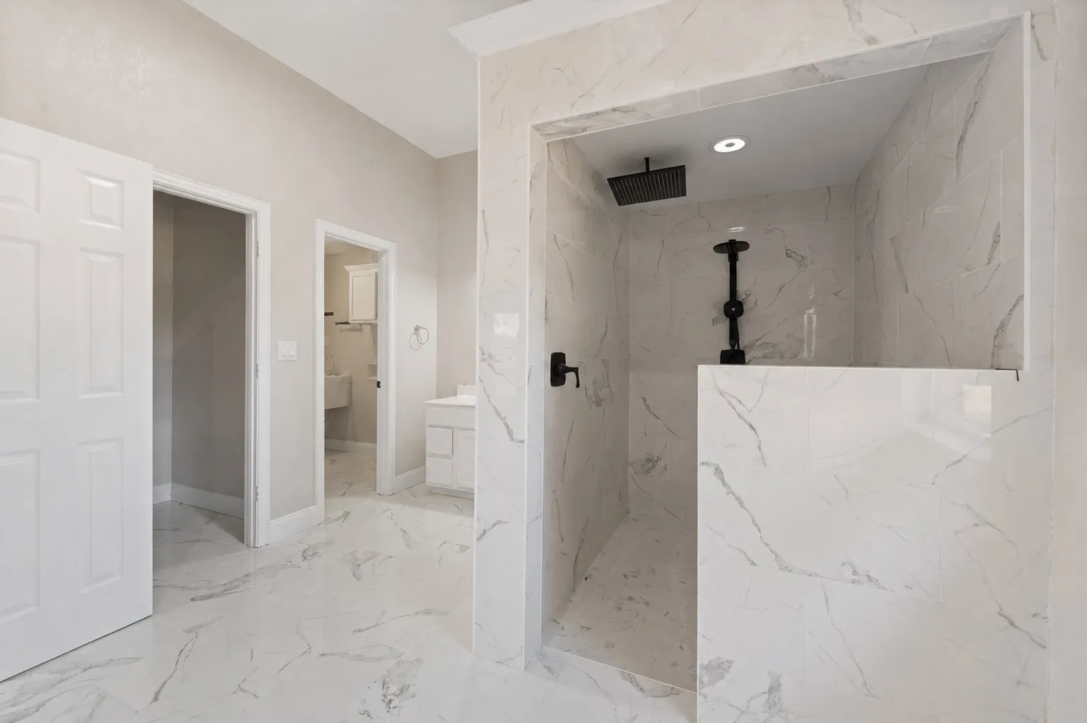Shower enclosure featuring white marbled tile, a rain shower head, and matte black fixtures