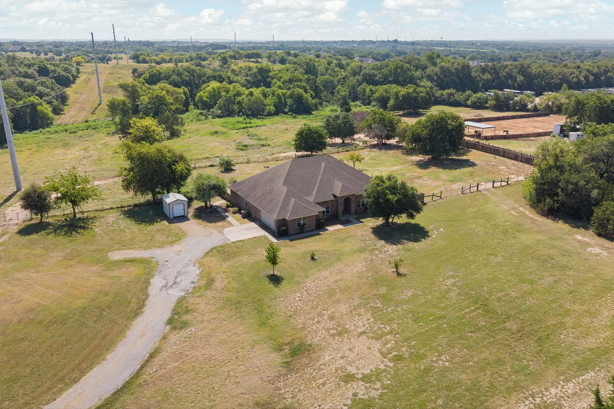 Expansive rural property featuring a brick residence with a dark shingle roof, a detached shed, and a gravel driveway
