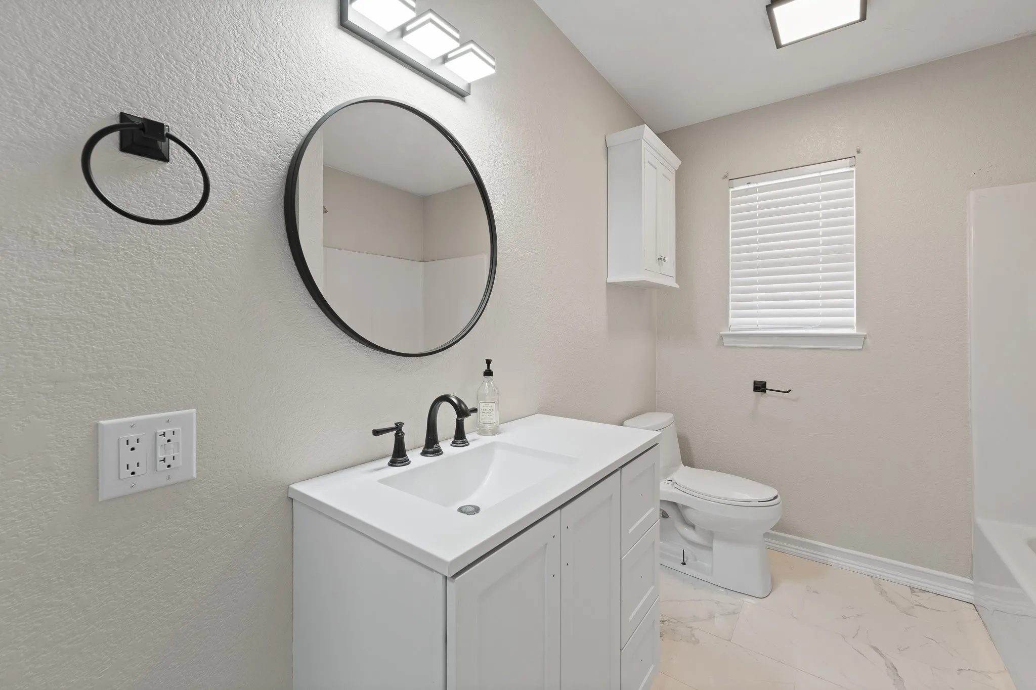 Modern bathroom featuring a white vanity with integrated sink, black-framed circular mirror, and matte black fixtures