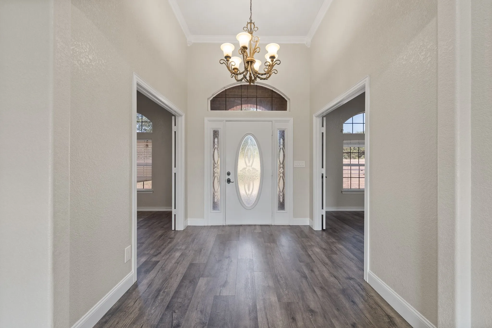 Grand entryway featuring wood-finish flooring, a decorative glass front door with sidelights and transom window, an ornate chandelier, and crown molding