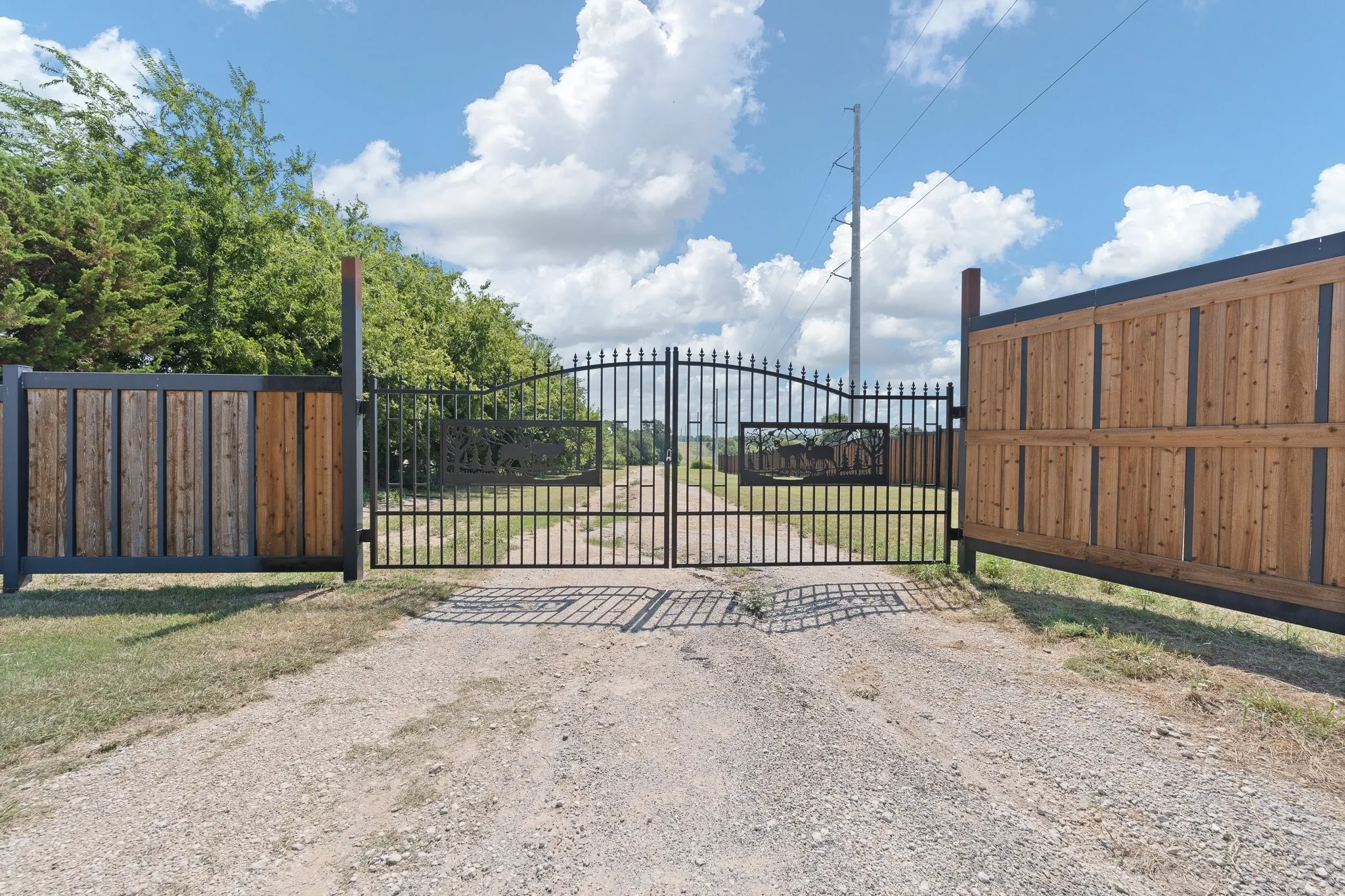 Wrought iron double gate entry with custom decorative inserts, flanked by wood-paneled fence sections with metal framing