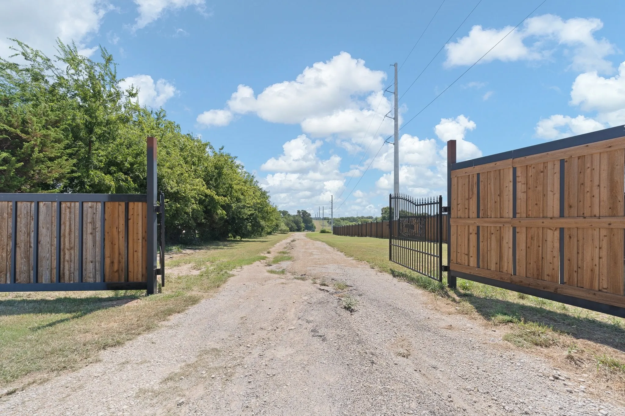 Gated entry featuring a gravel drive, wood and metal panel gates, and a wrought iron entry gate