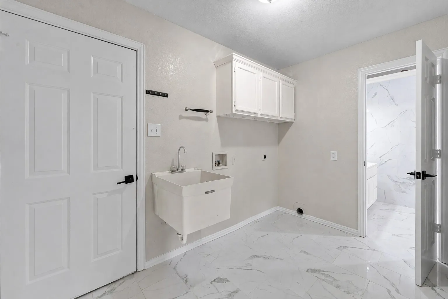 Utility room featuring white shaker-style cabinetry, a wall-mounted utility sink, and white marble-look flooring