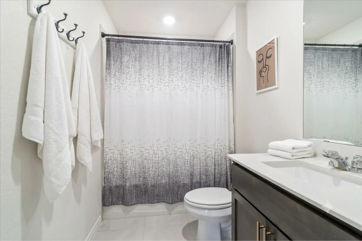 Bathroom featuring a dark wood-finish vanity with a white countertop and integrated sink, a large wall-mounted mirror, a commode, and light-toned tile flooring