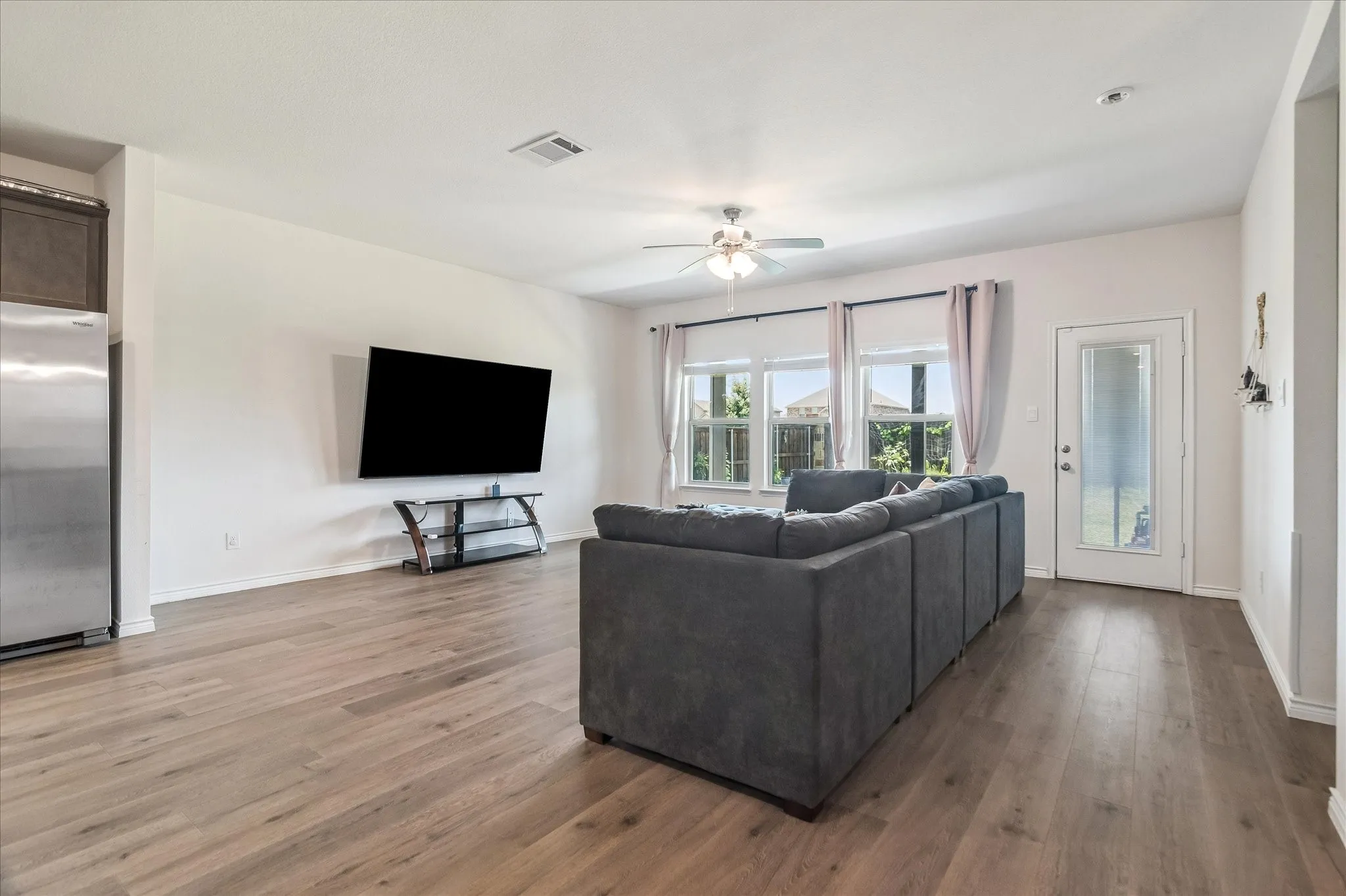 Spacious living area featuring wood-finish flooring and ample natural light from multiple windows