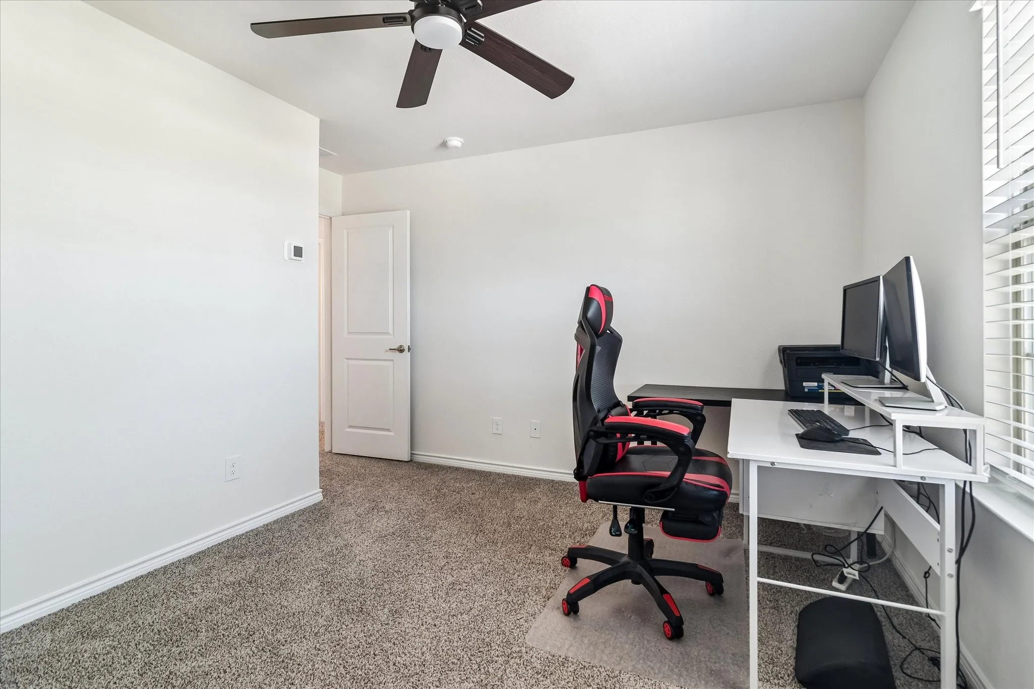 Bright room featuring neutral-toned carpet flooring, white walls, a window with horizontal blinds, and an overhead ceiling fan