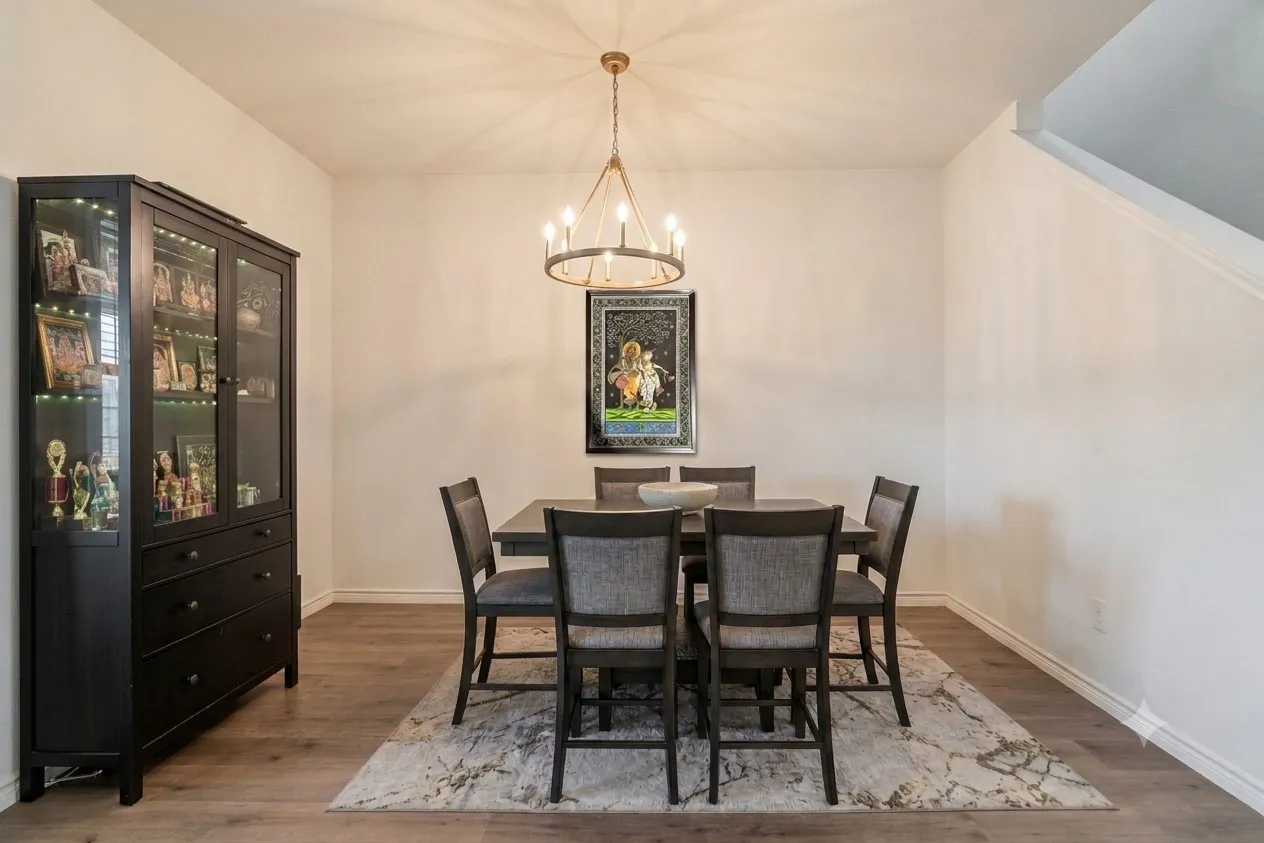 Dining area featuring wood-finish flooring, a contemporary chandelier, and a built-in display cabinet with interior lighting