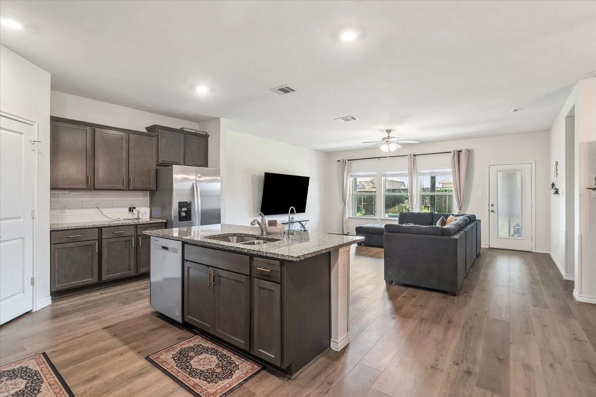 Kitchen featuring gray shaker-style cabinetry, stainless steel appliances, granite countertops, a subway tile backsplash, and wood-finish flooring