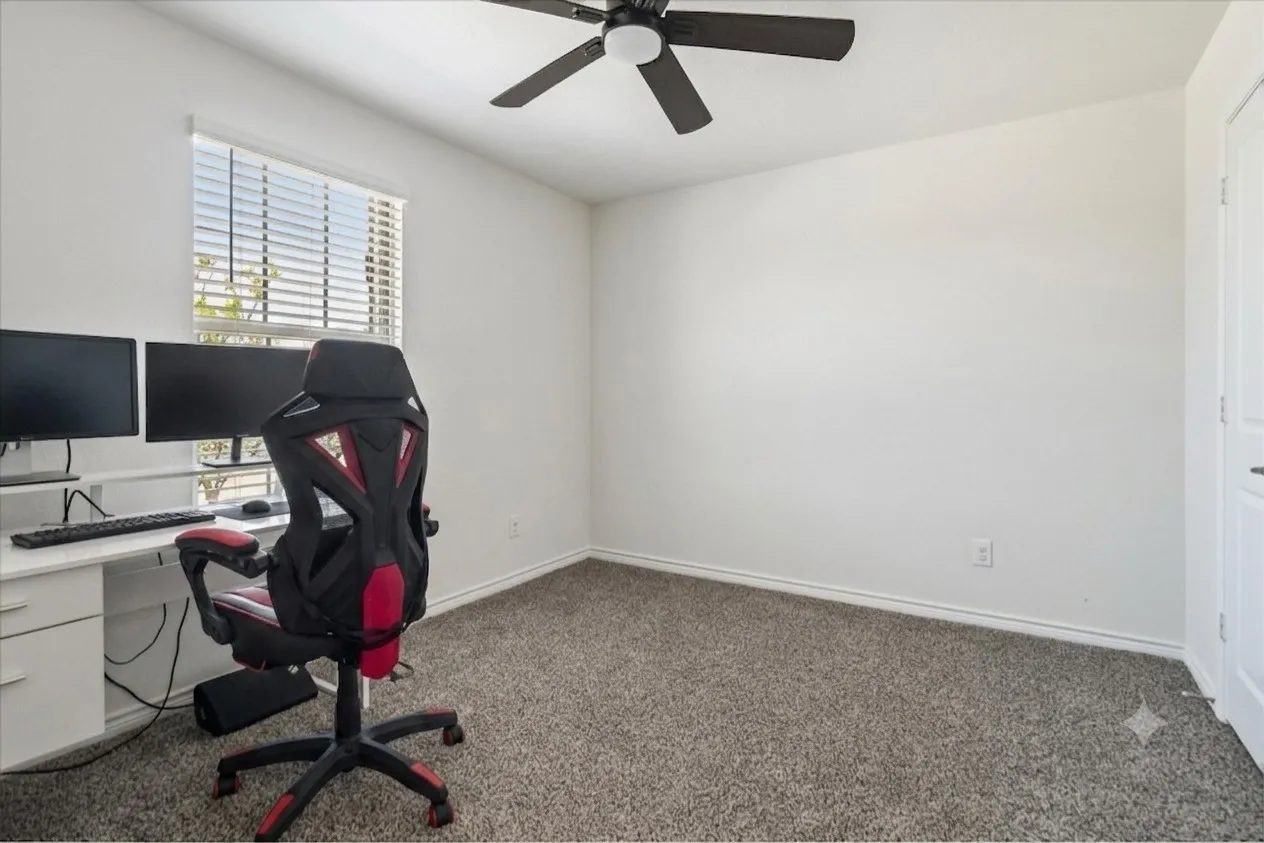Bright room featuring neutral-toned carpet flooring, white walls, a window with horizontal blinds, and an overhead ceiling fan