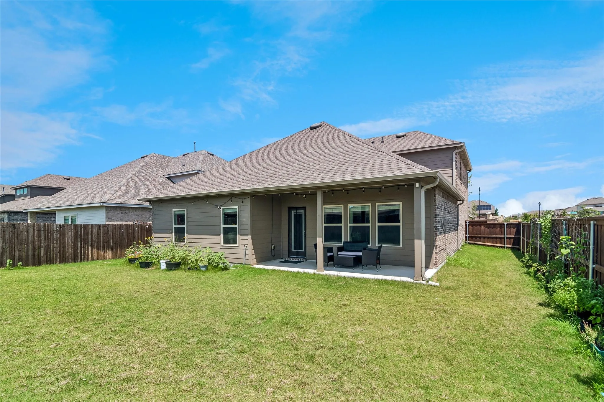 Expansive backyard featuring a covered patio, a spacious lawn area, durable wood fencing, and an exterior with siding and stone accents