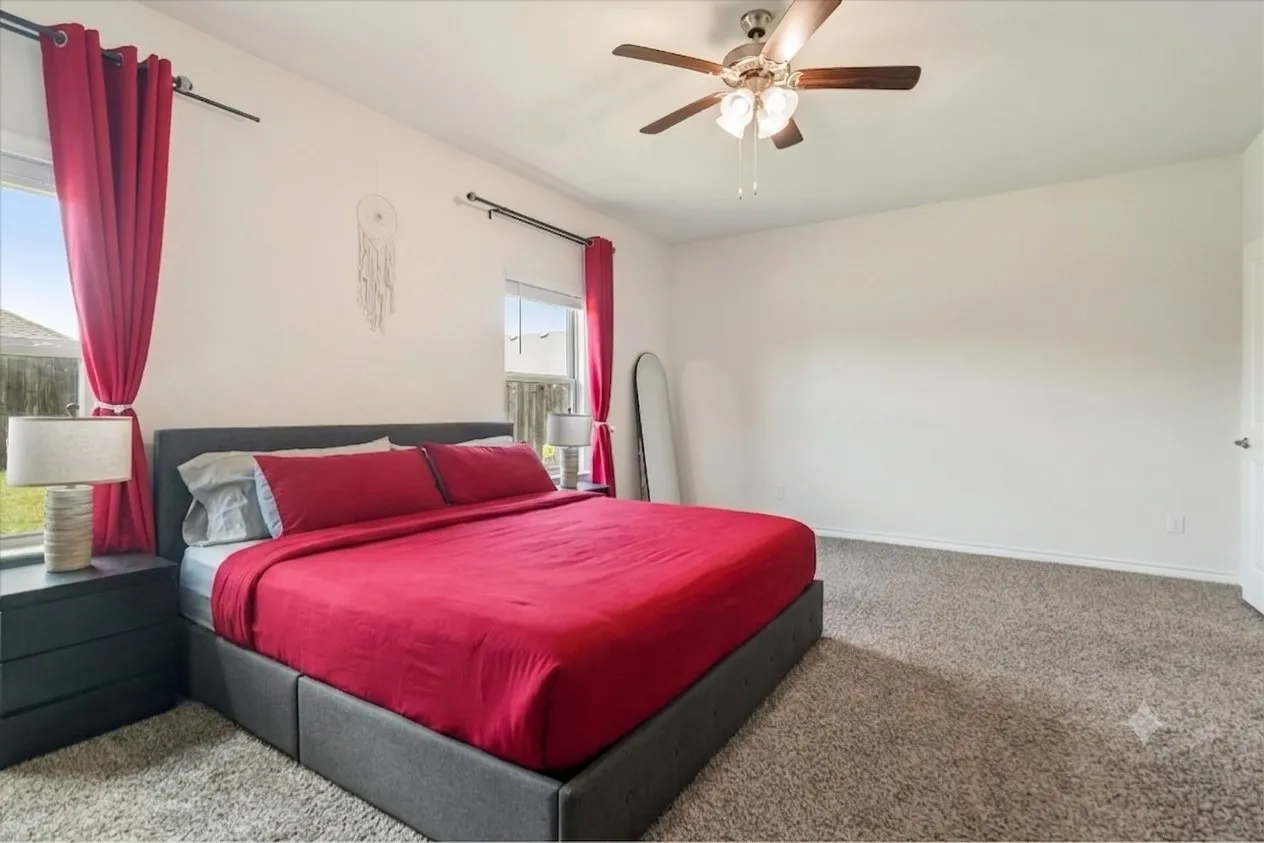 Carpeted room featuring a ceiling fan with integrated lighting, two windows, and a white paneled door