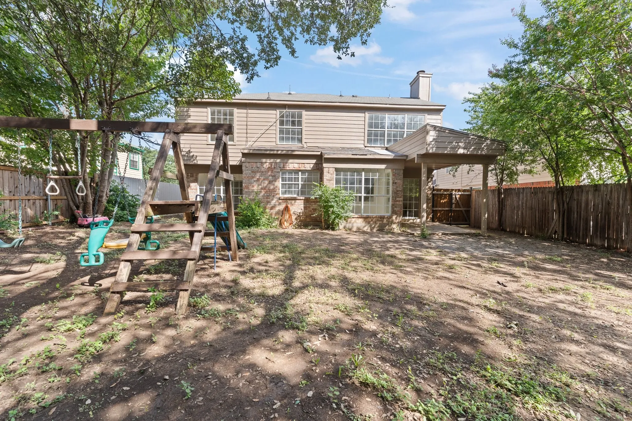 Expansive backyard featuring a covered patio, a full privacy fence, and mature trees providing shade