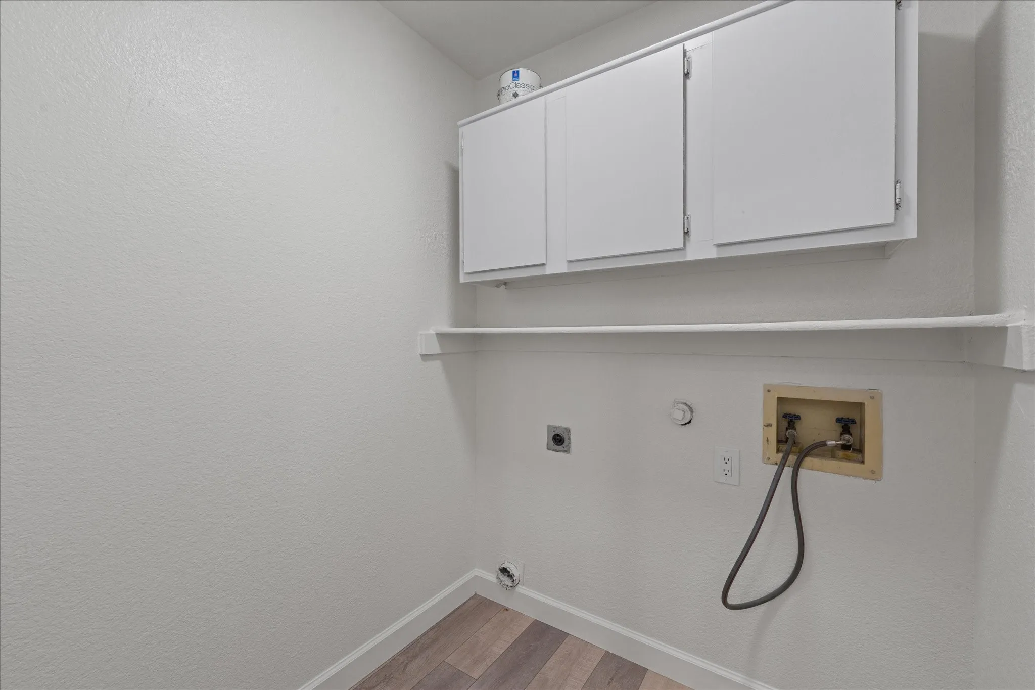 Dedicated utility space featuring overhead white cabinetry, wood-finish flooring, and wall-mounted shelving